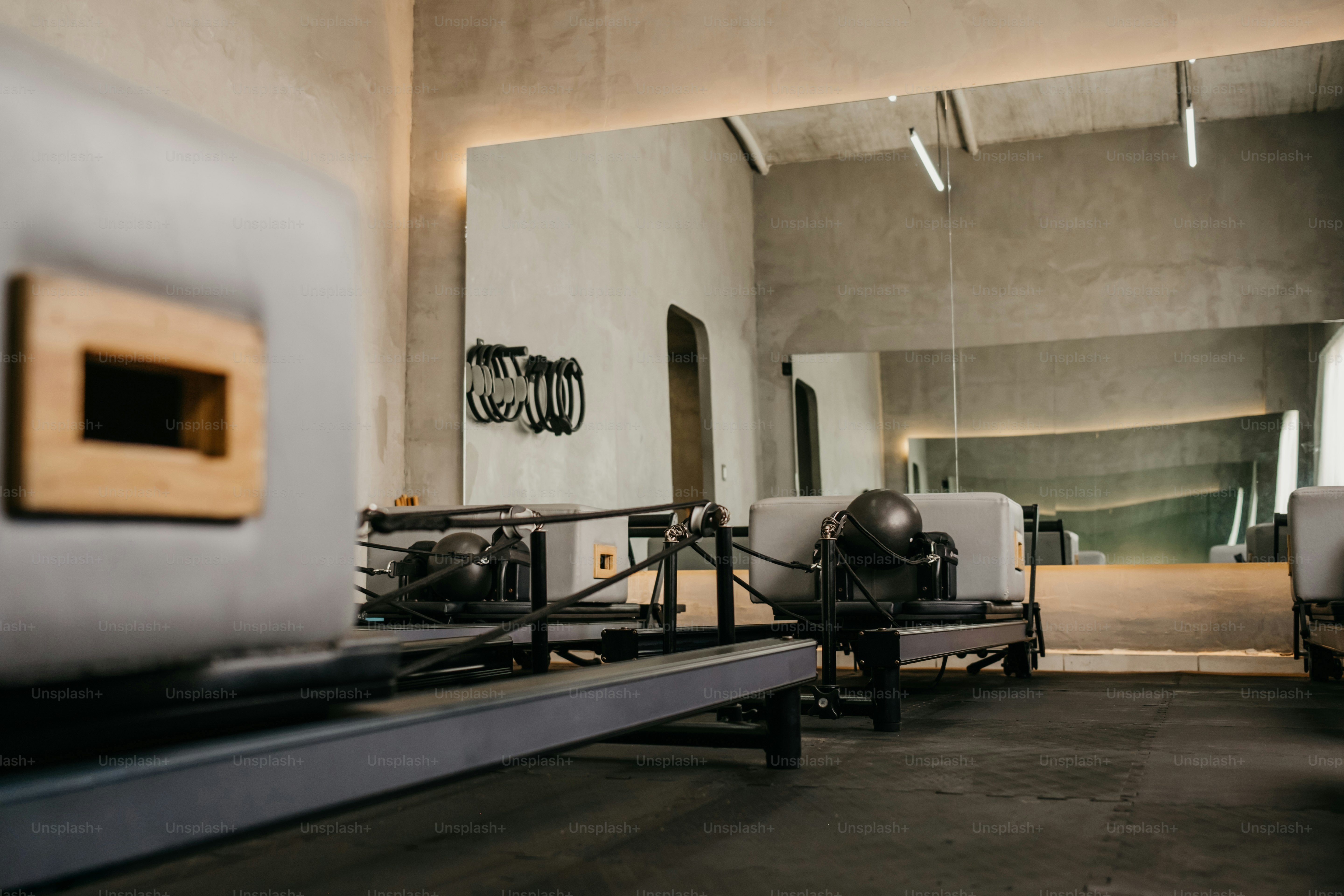 Pilates-Reformer in einem minimalistischen Studio mit Betonwänden und einem großen Spiegel