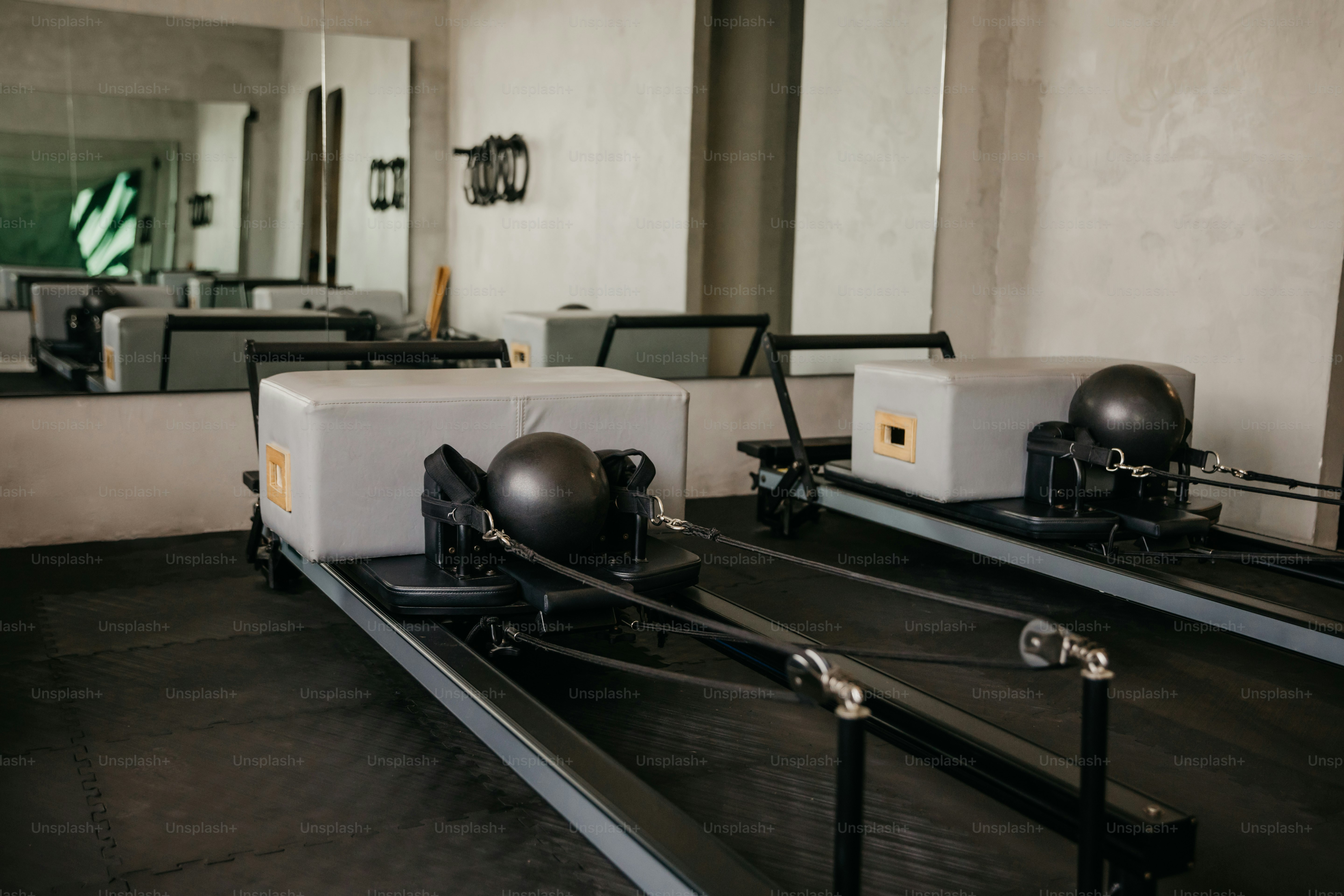 Zwei Pilates-Reformer mit grauen Schachteln und schwarzen Bällen in einem Studio