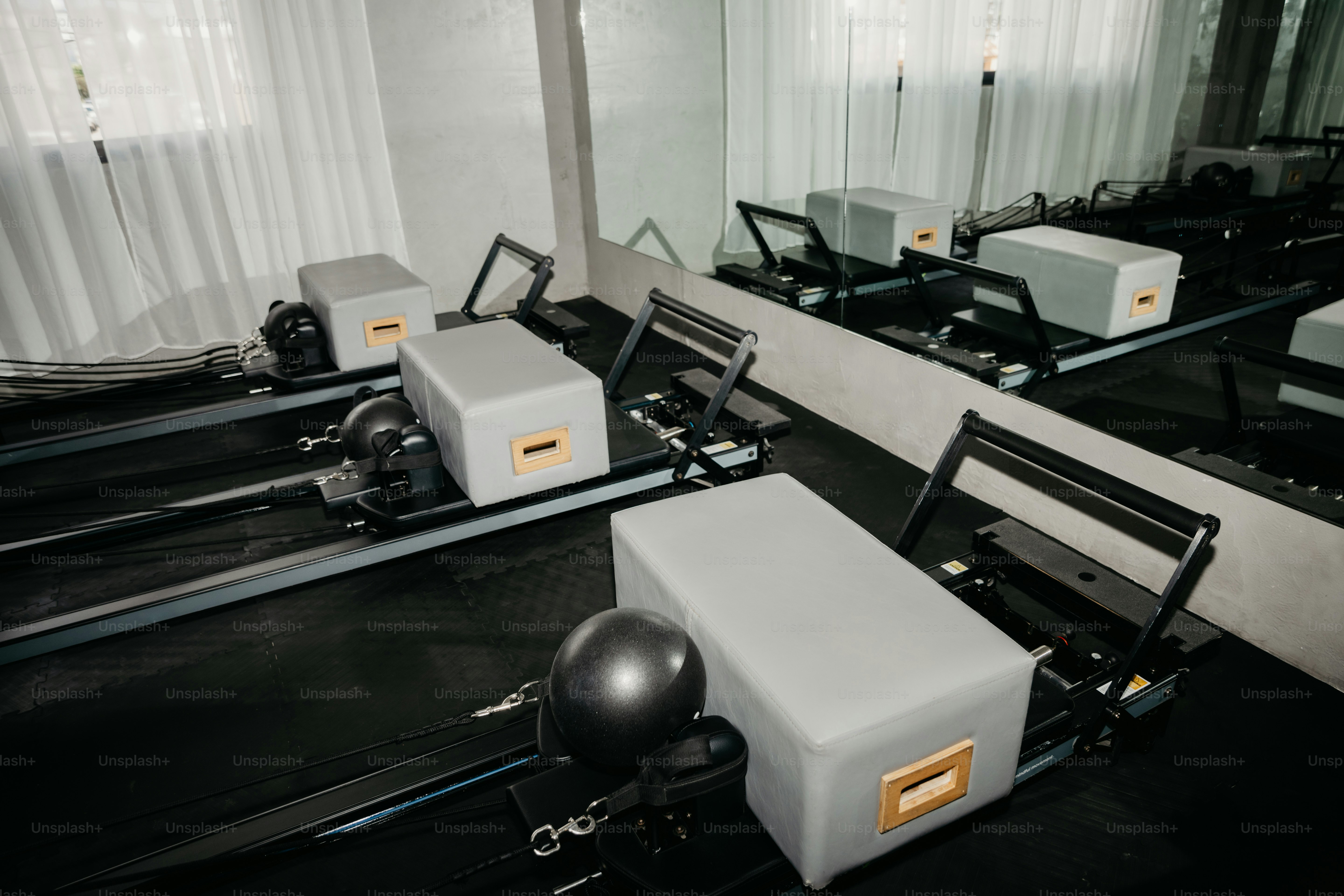 Pilates-Reformer mit grauen Schachteln und schwarzen Bällen in einem Studio mit Spiegeln