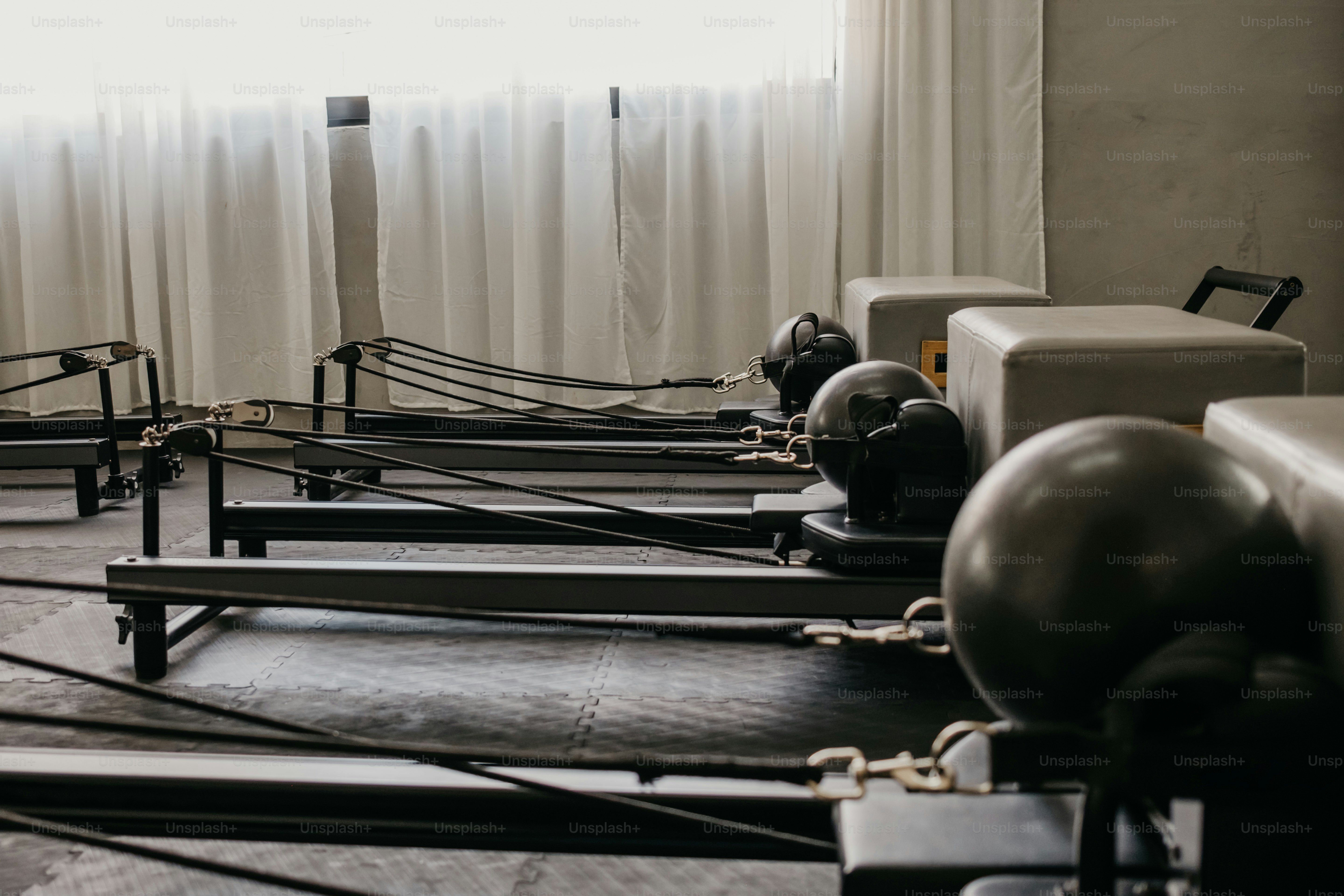 Mehrere Pilates-Reformer mit grau gepolsterten Boxen in einem sonnenbeschienenen Studio