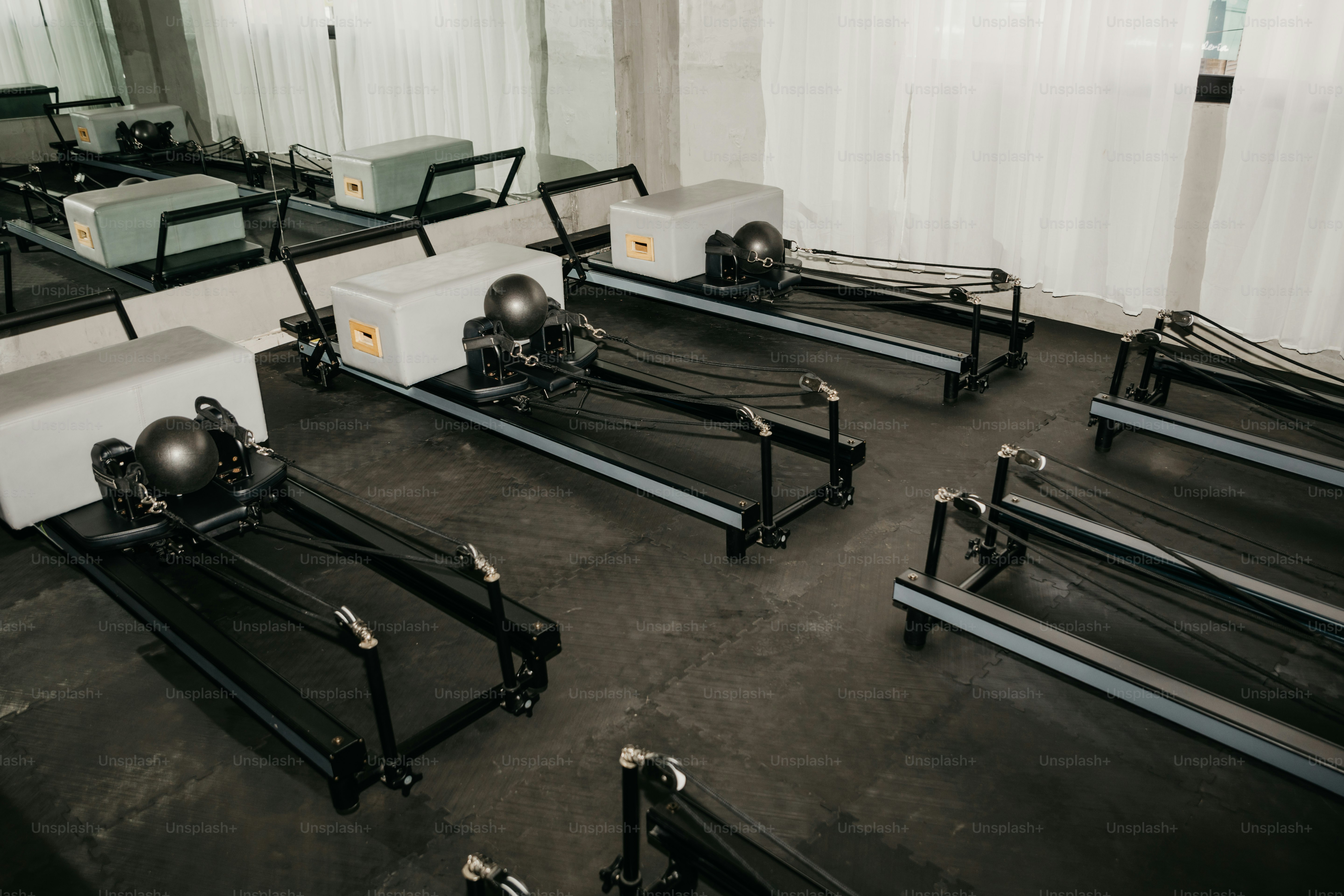 Mehrere Pilates-Reformer mit grau gepolsterten Boxen in einem hellen Studio