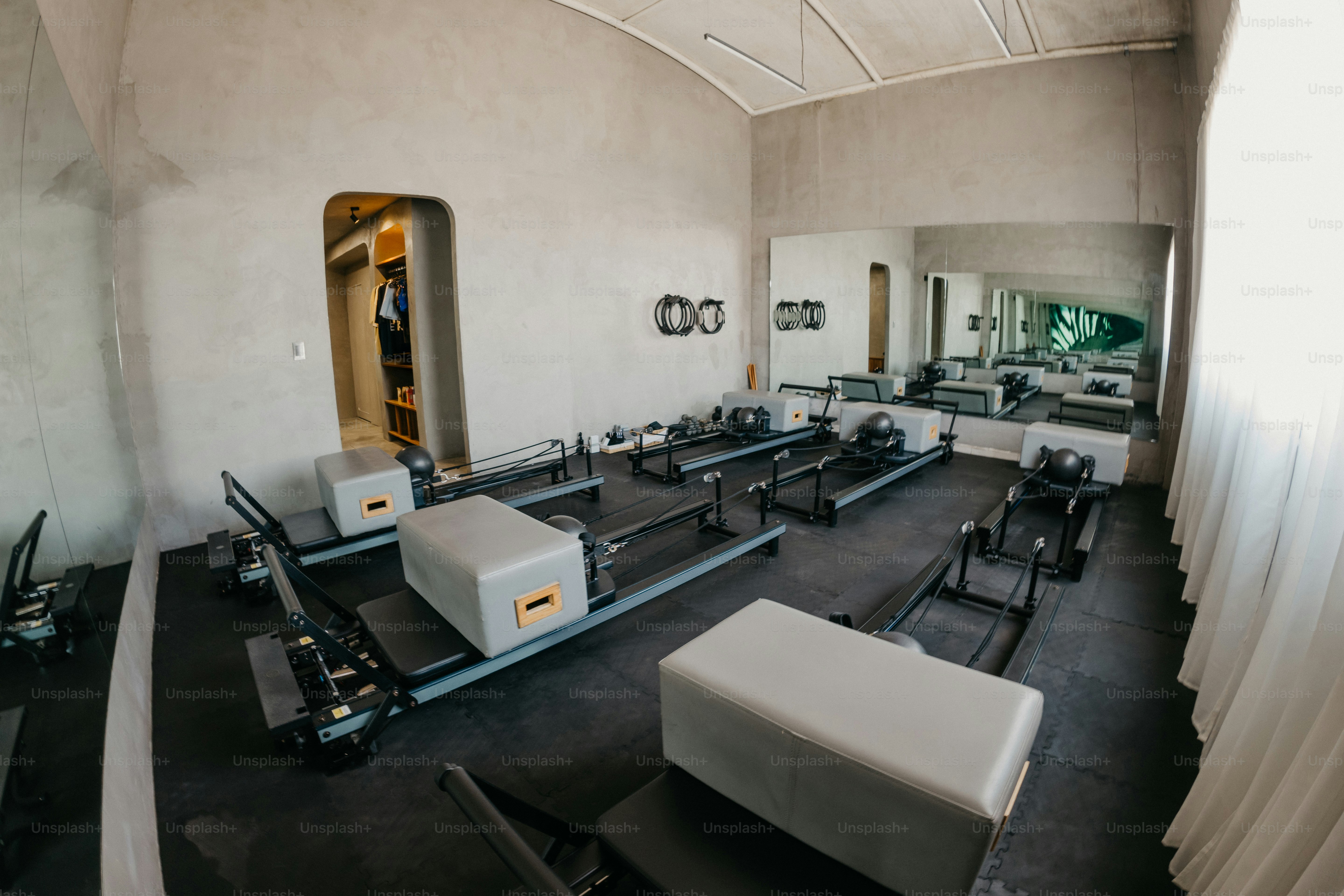 Mehrere Pilates-Reformer in einem minimalistischen Studio mit Betonwänden und schwarzem Boden