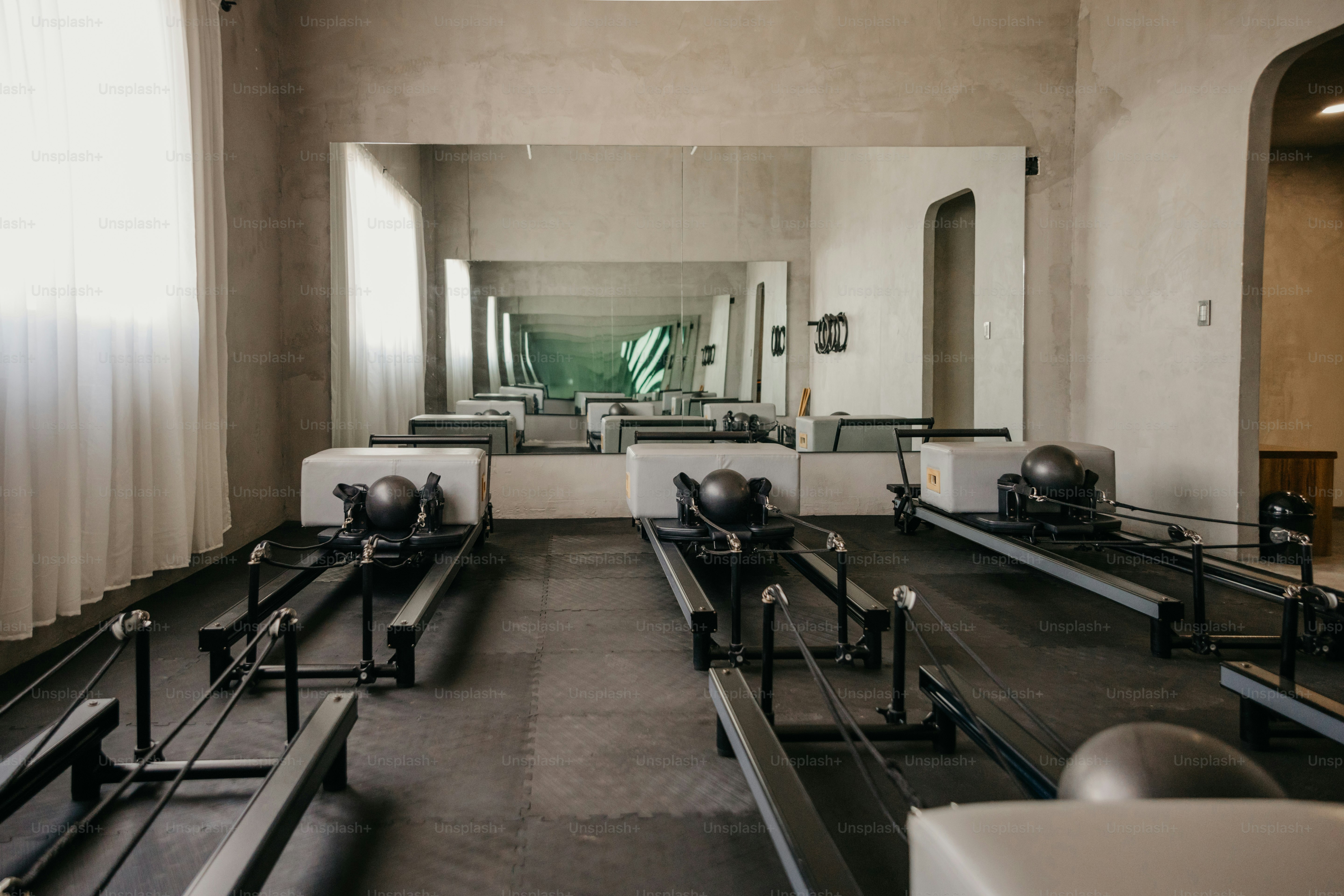 Drei Pilates-Reformer mit grauen Schachteln und schwarzen Bällen in einem minimalistischen Studio