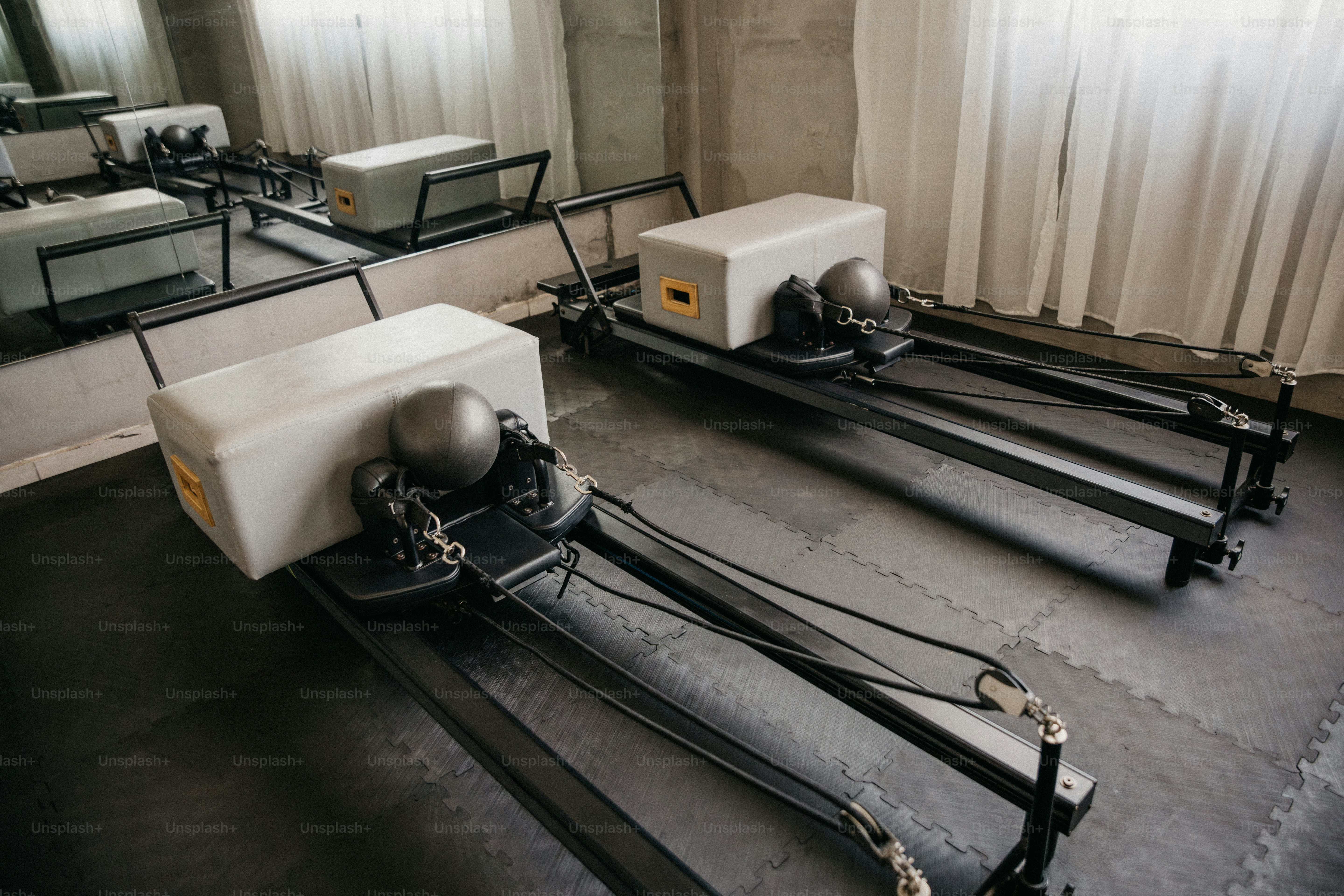 Zwei Pilates-Reformer mit grauen Kisten und Bällen in einem sonnenbeschienenen Studio