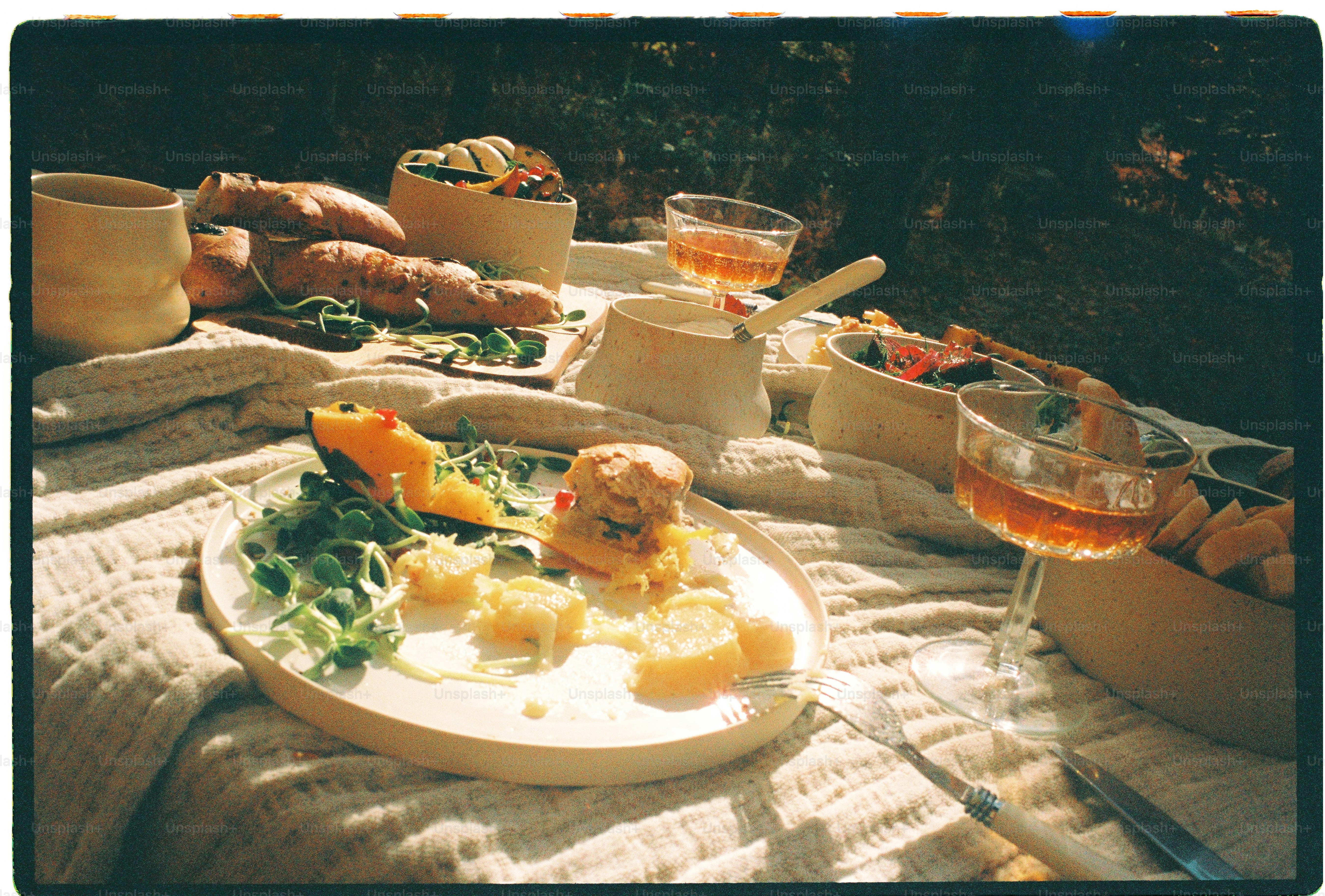 Un picnic scoperto con pane, insalata e bevande su un tessuto texturizzato all'aperto