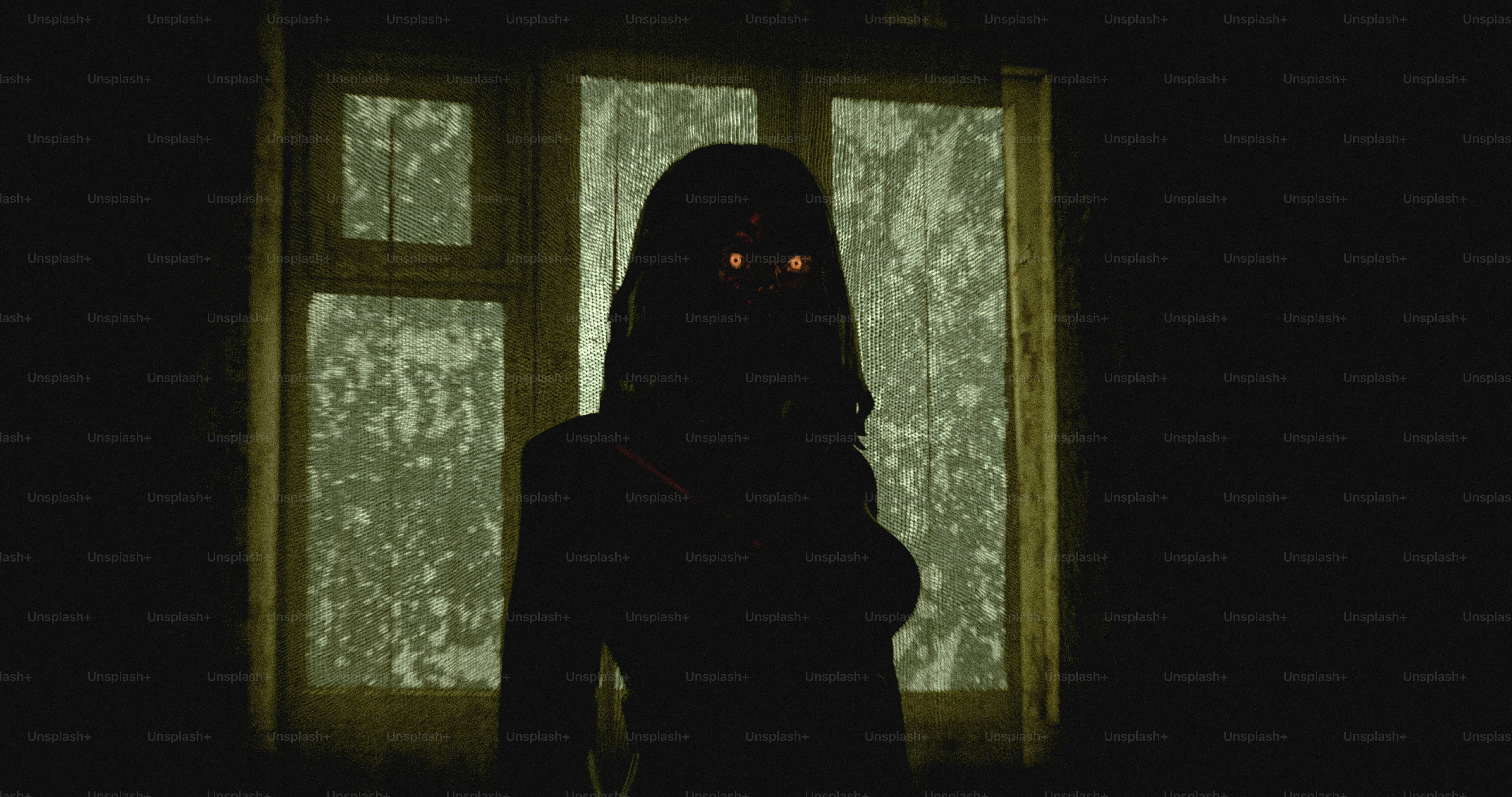 A person in silhouette with glowing eyes against a window with a mesh screen