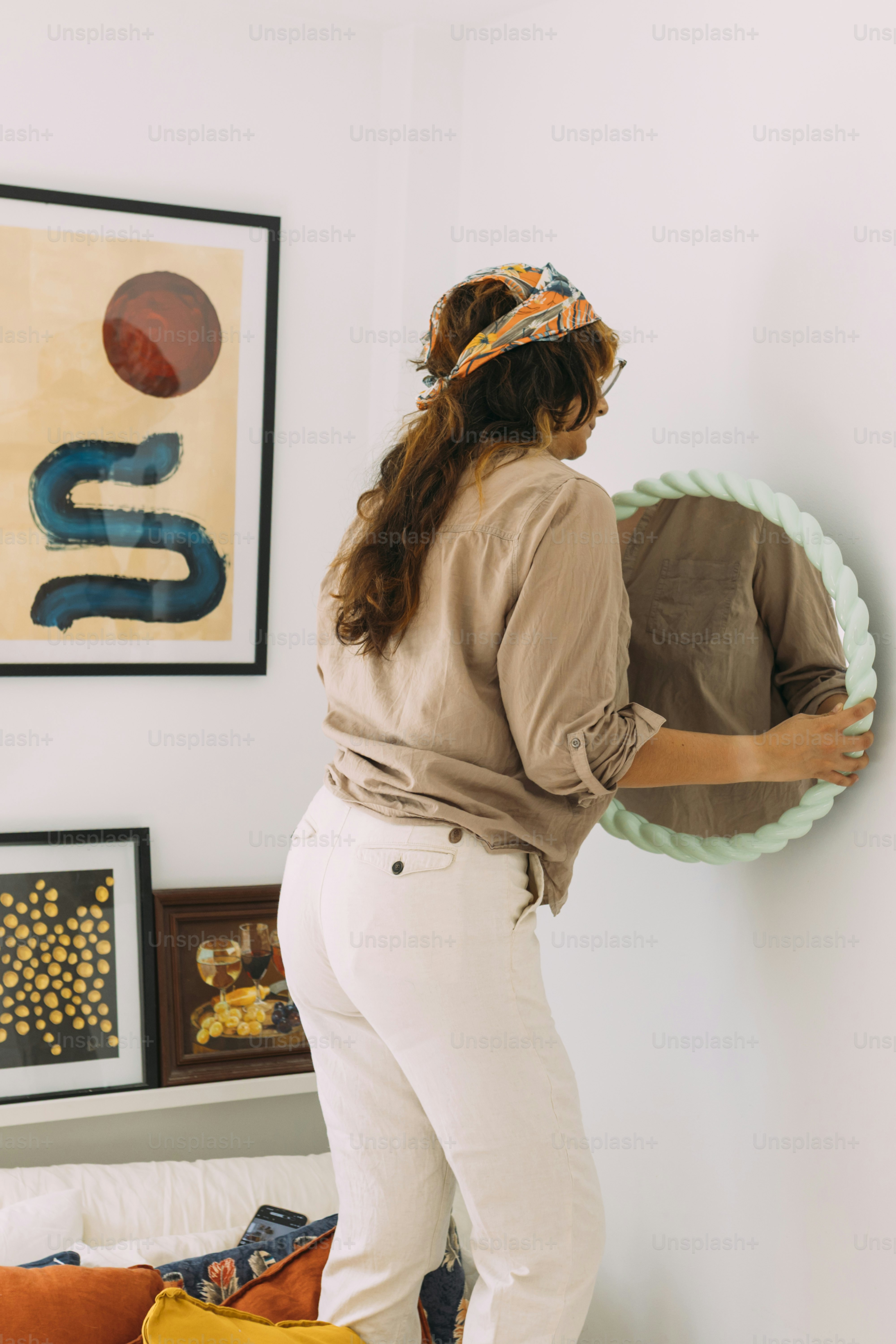 A woman in a tan shirt and headscarf adjusting a round mirror on a wall
