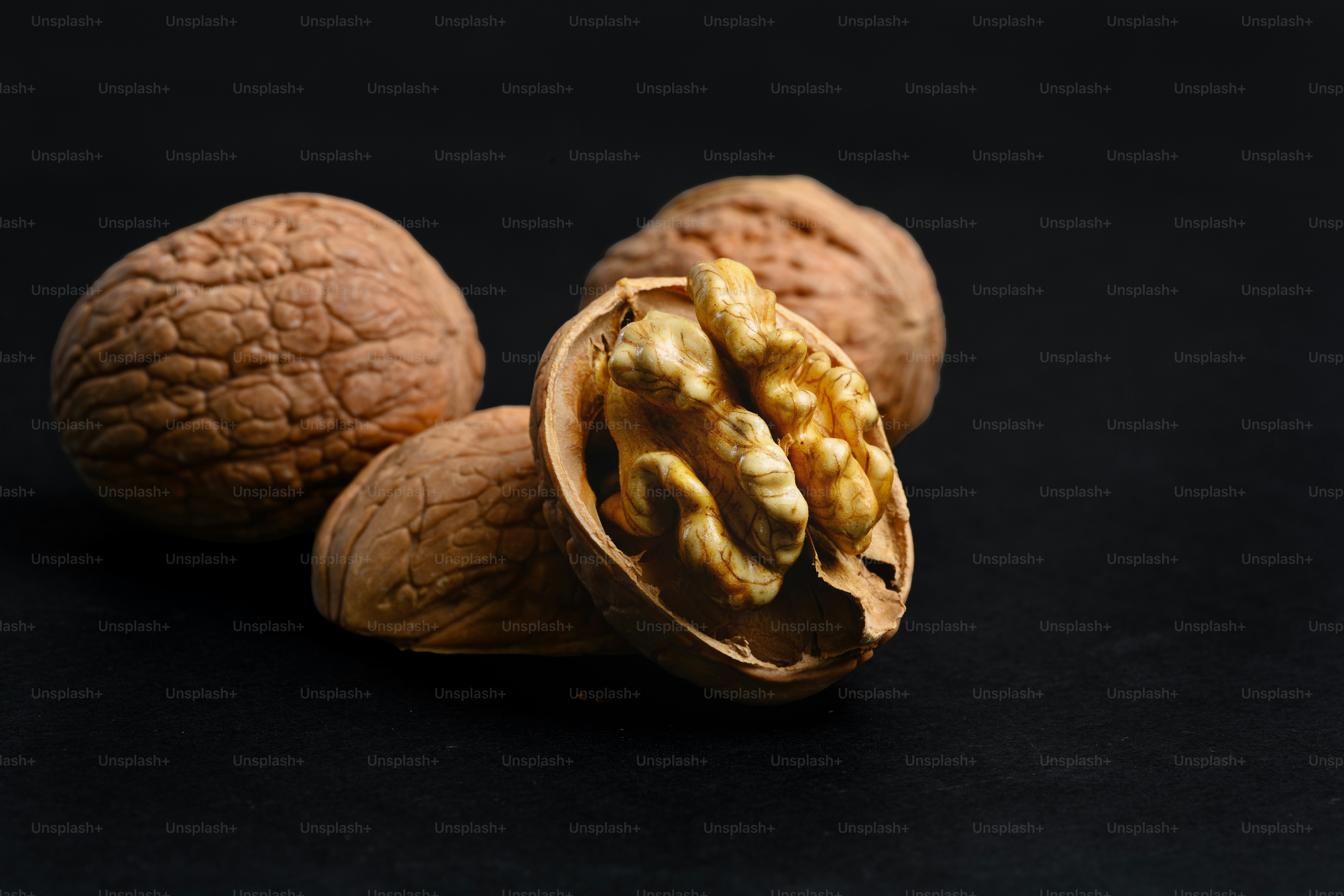A whole walnut and a cracked walnut with a visible kernel on black