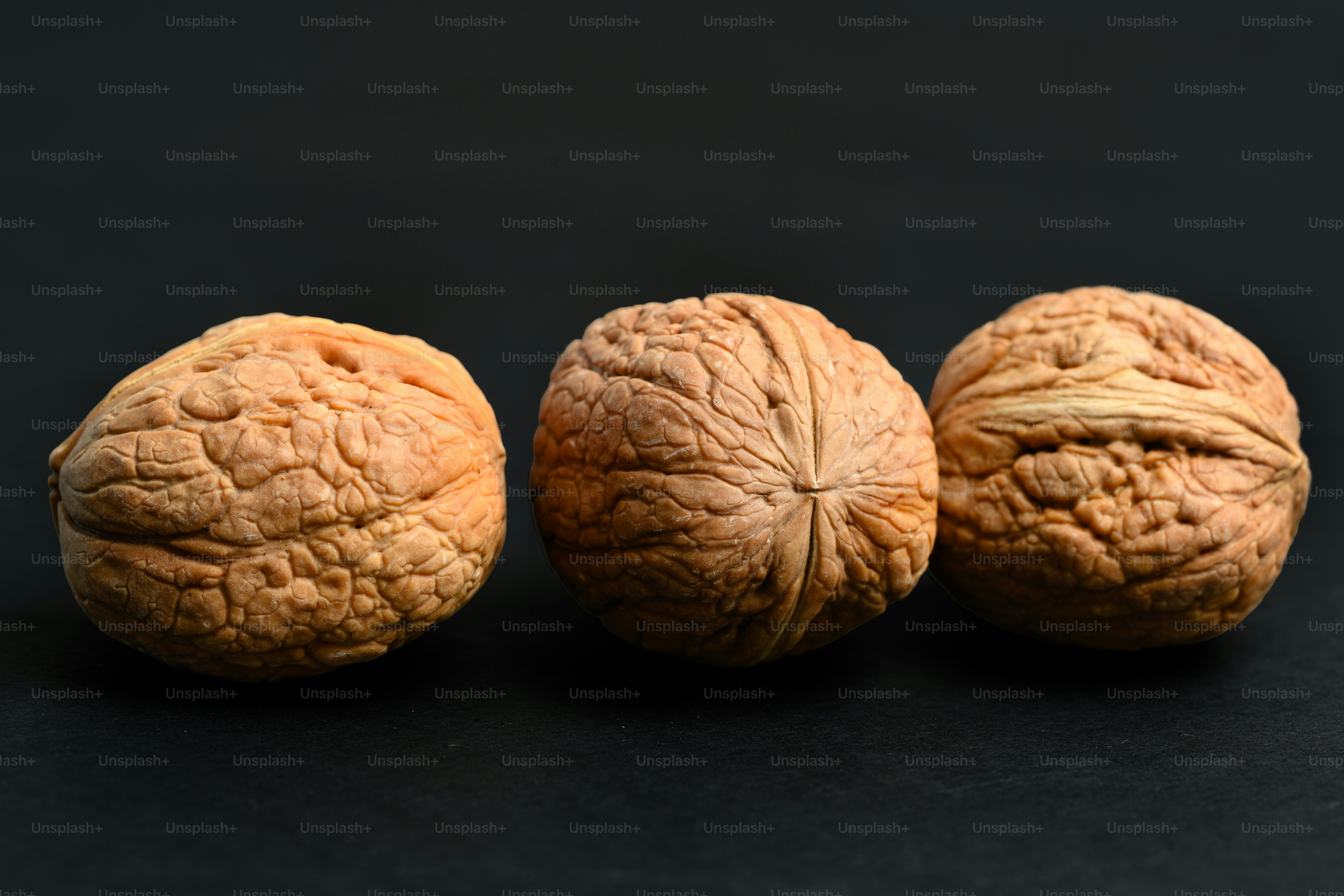Three whole walnuts with textured brown shells on a dark surface