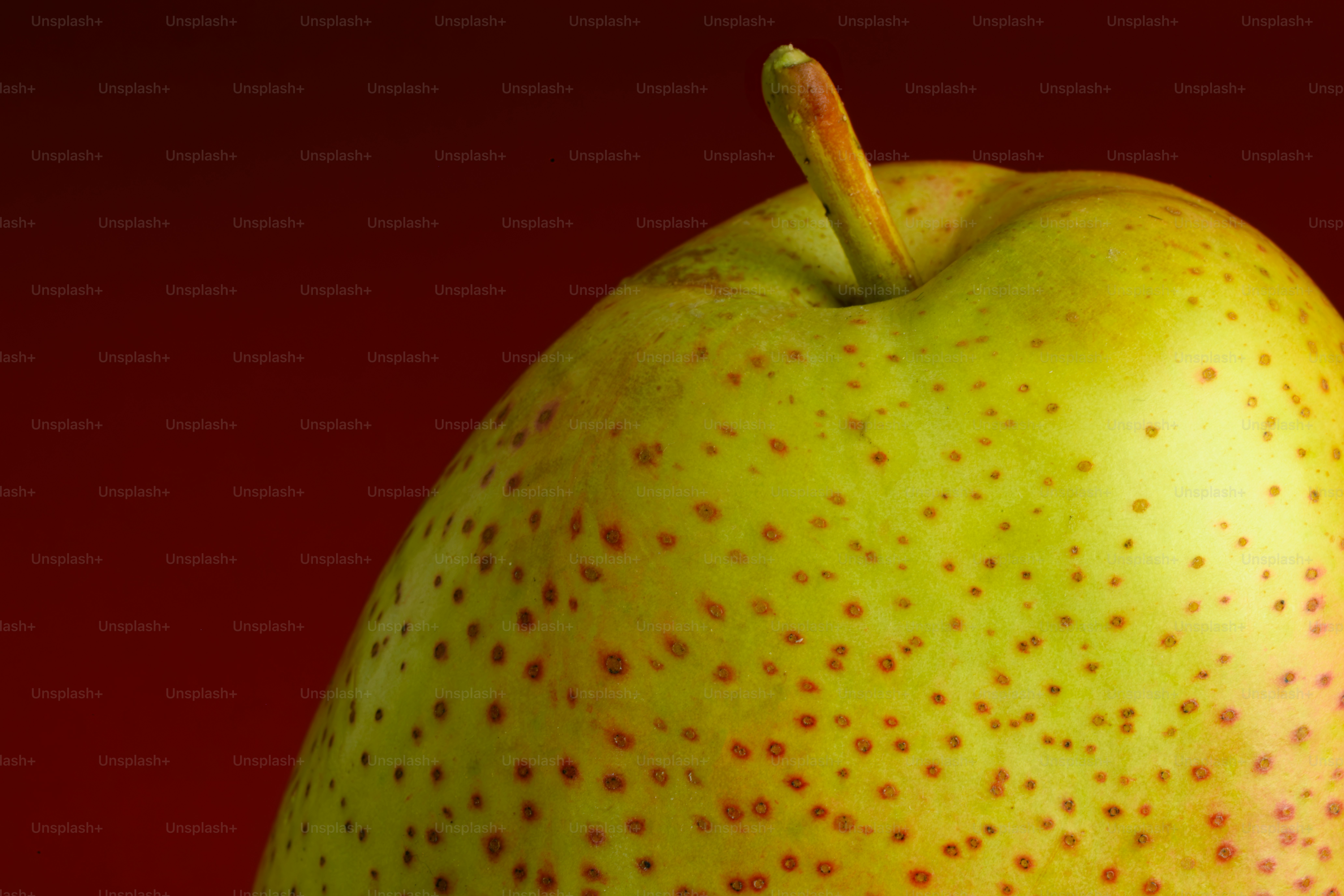 A close-up of a yellow pear with brown spots against a dark background