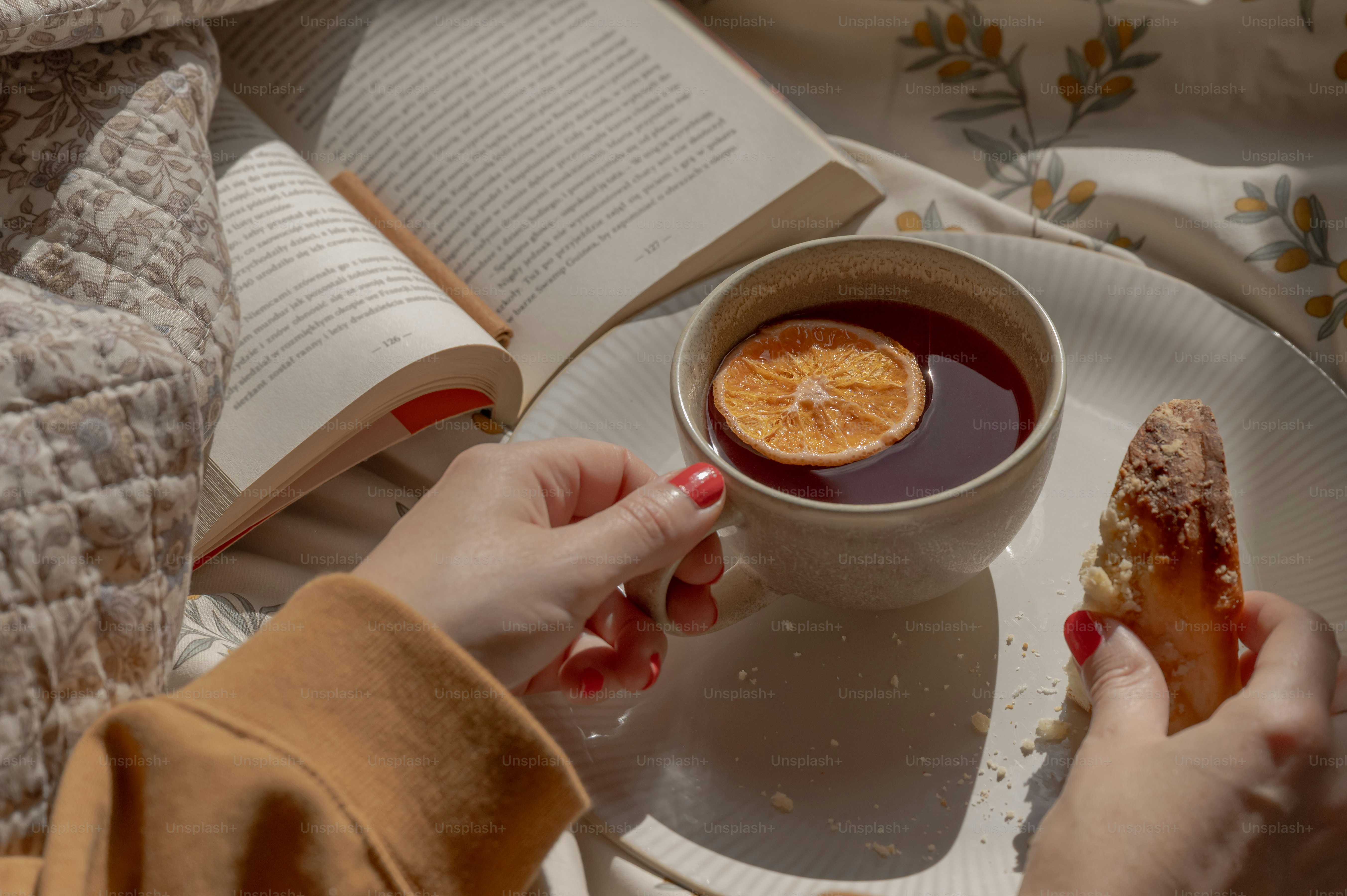 A person holding a cup of tea with a dried orange slice and pastry