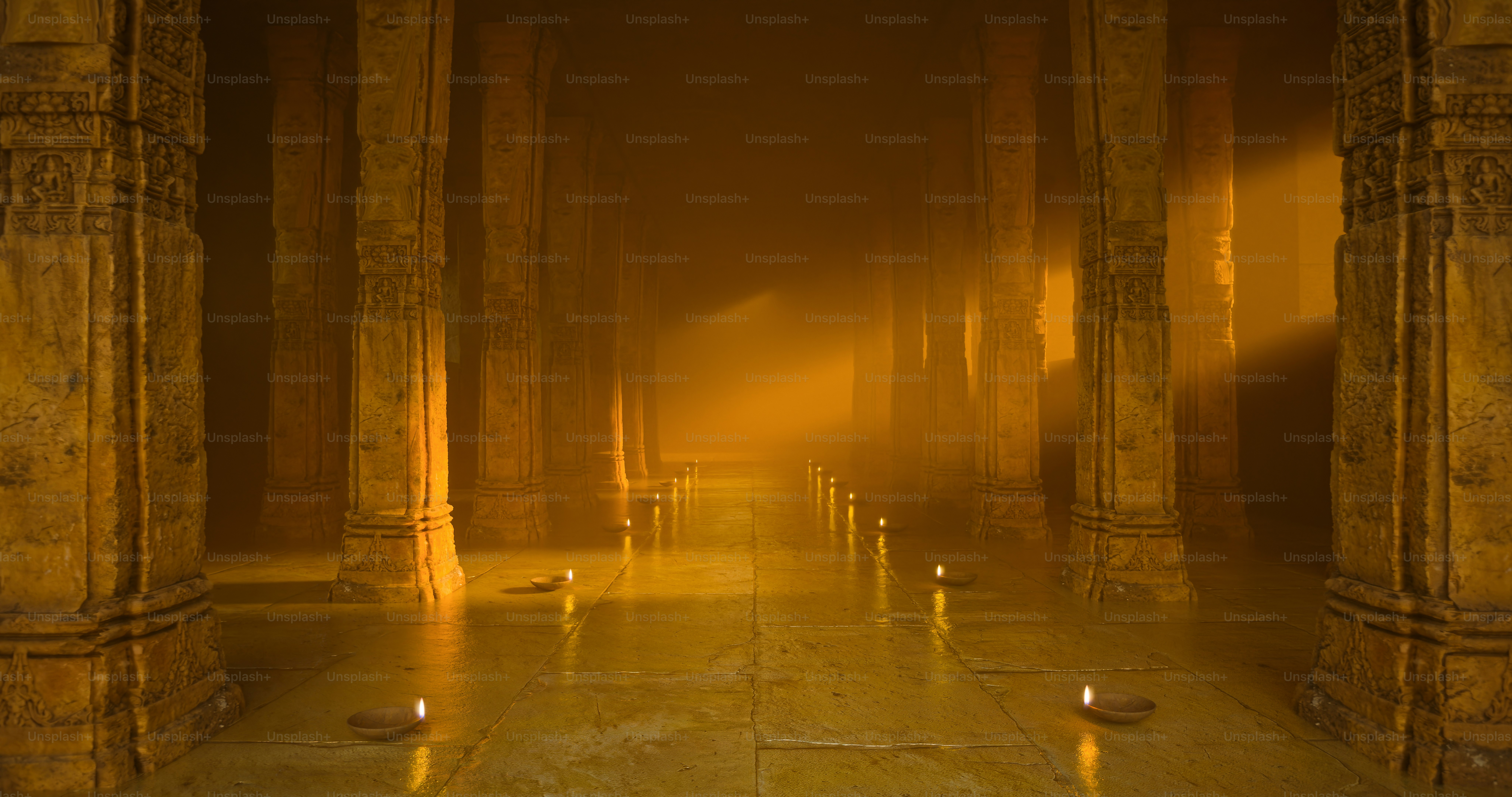 Stone pillars in a dimly lit temple hall with small oil lamps on floor