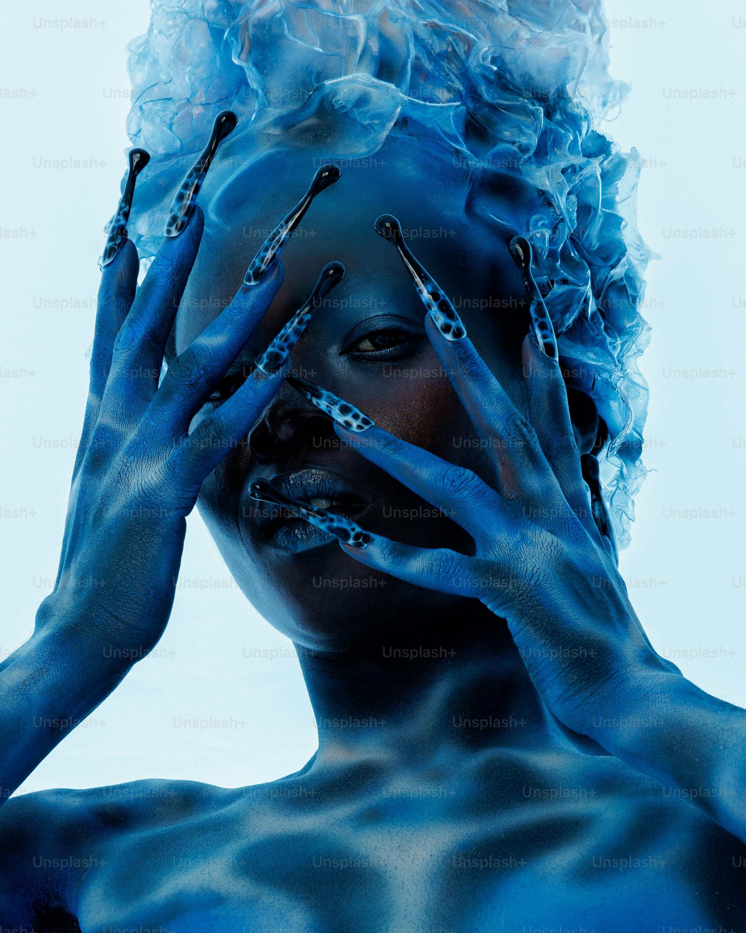 A person with blue skin and long patterned nails covering their face