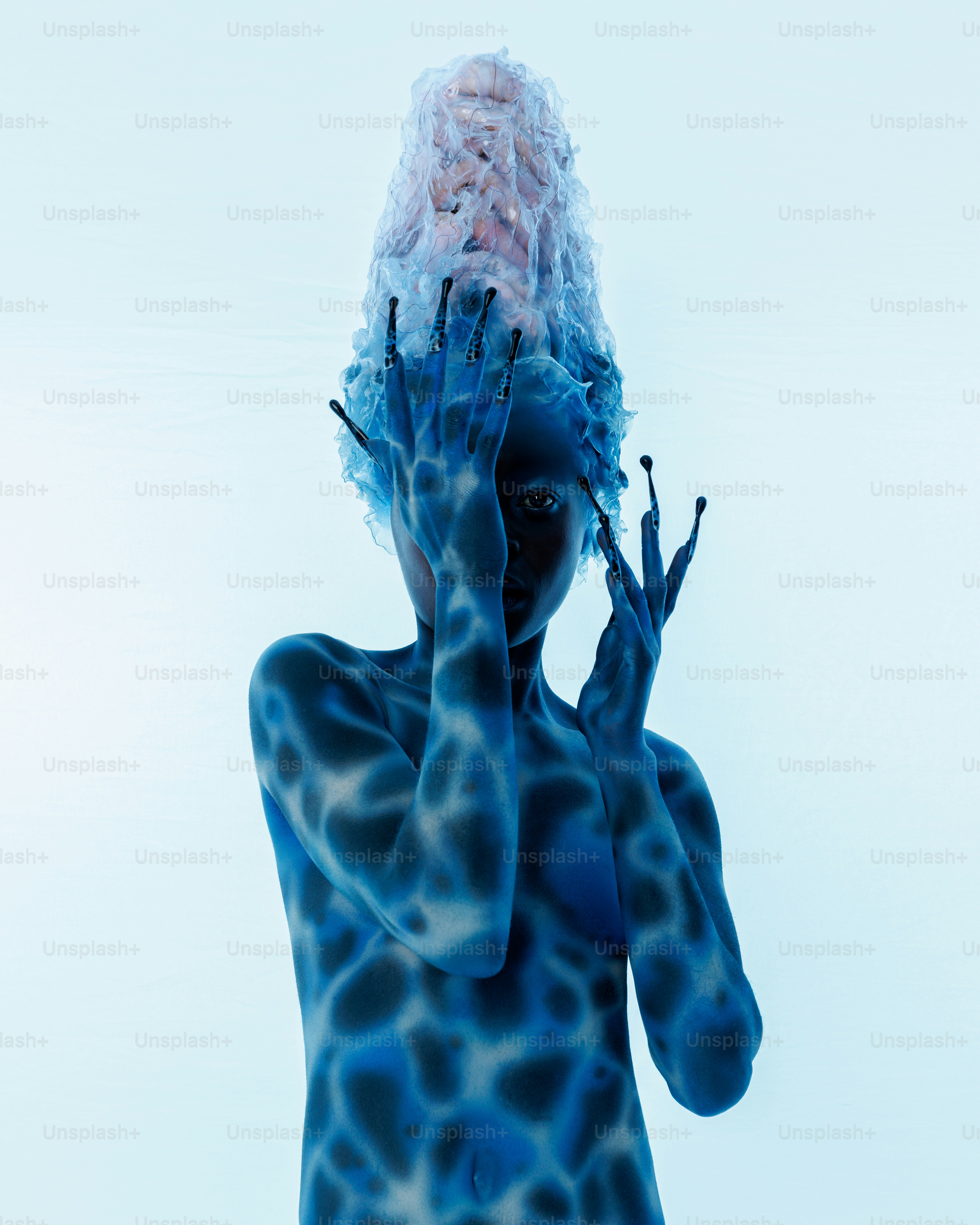 A person with blue skin and dark spots wearing a clear plastic headpiece