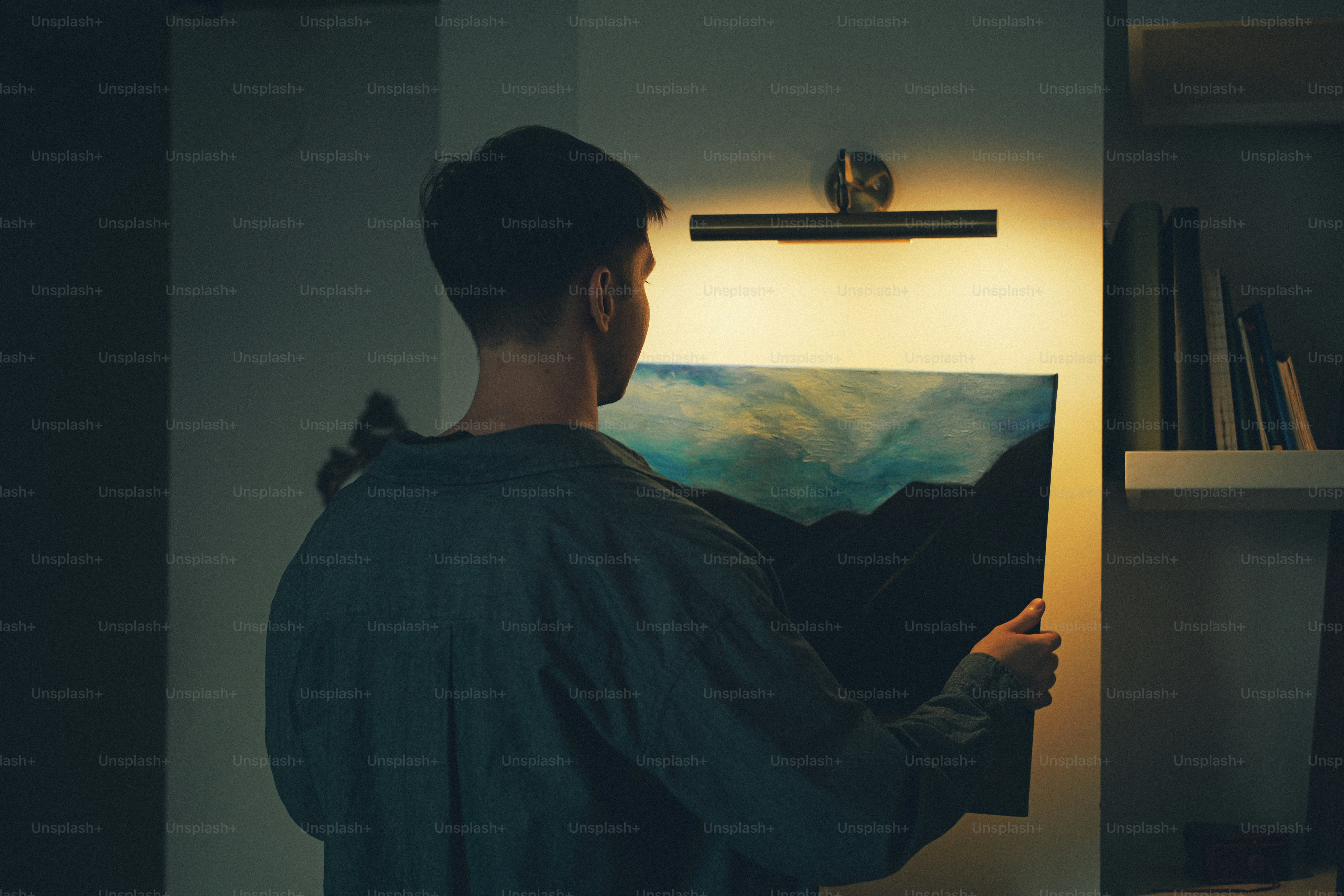 A person in a dark shirt hanging a landscape painting on a wall