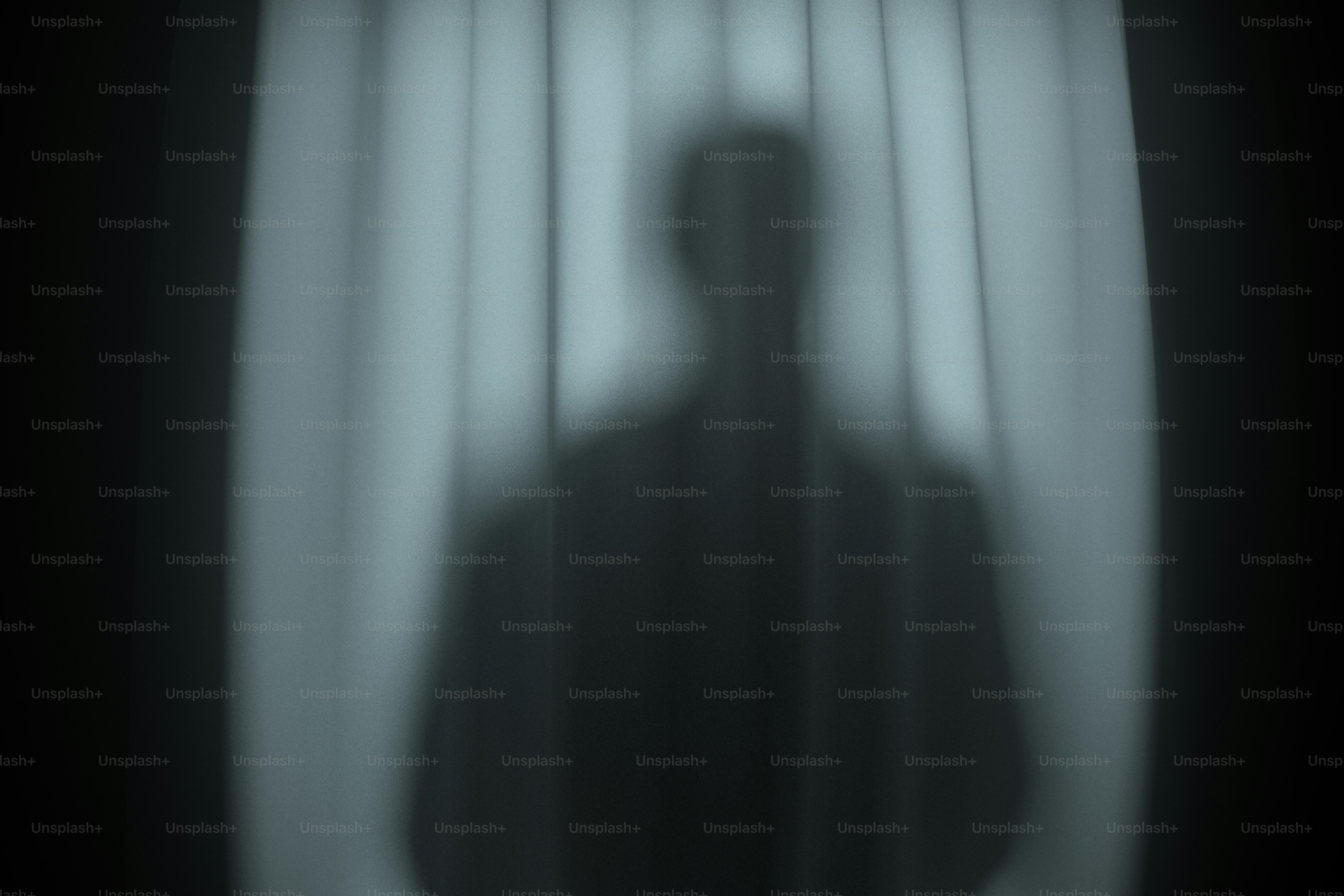 A dark silhouette of a person behind a translucent white curtain