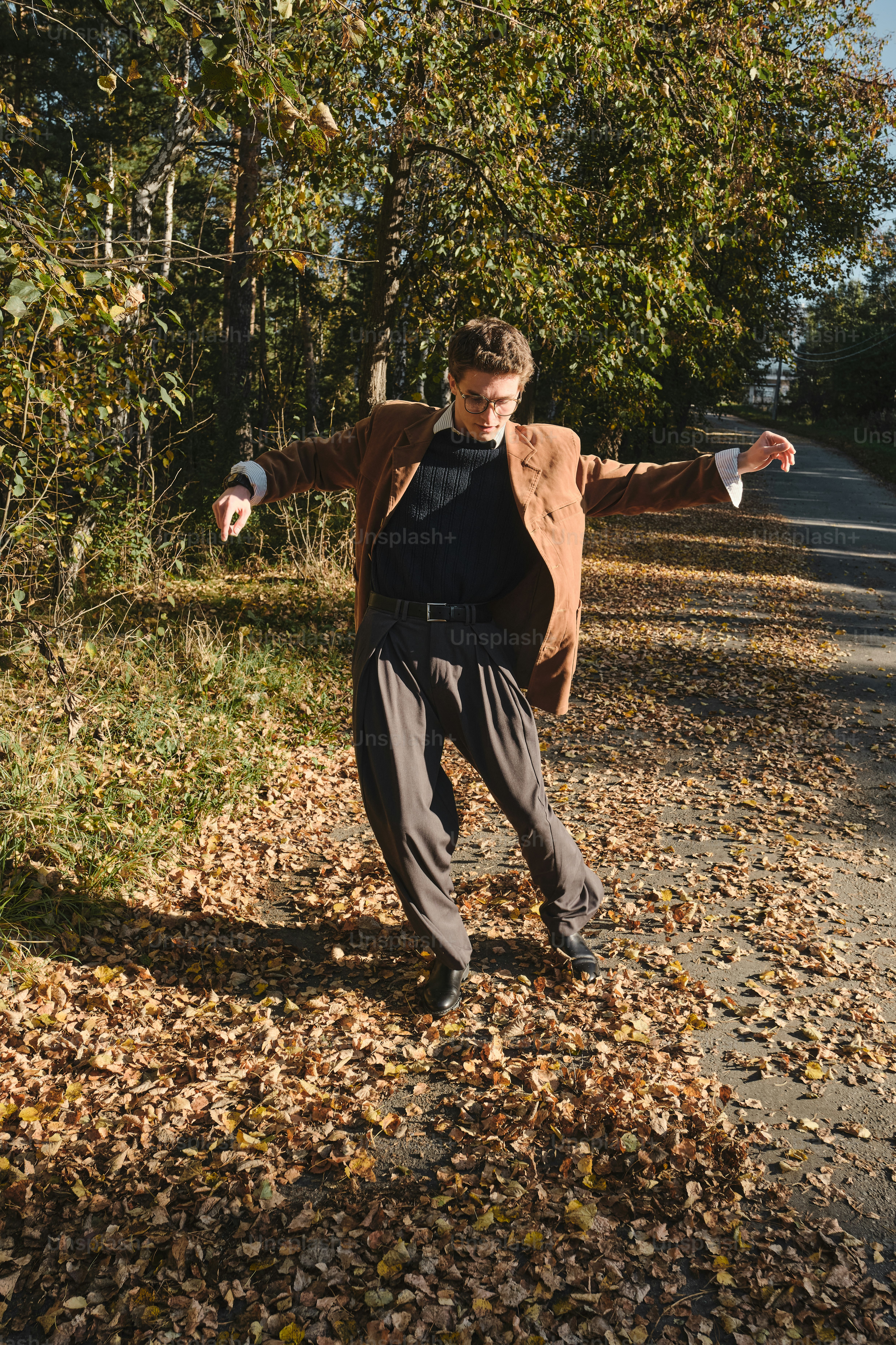 A person in a brown blazer and grey trousers dancing on fallen autumn leaves
