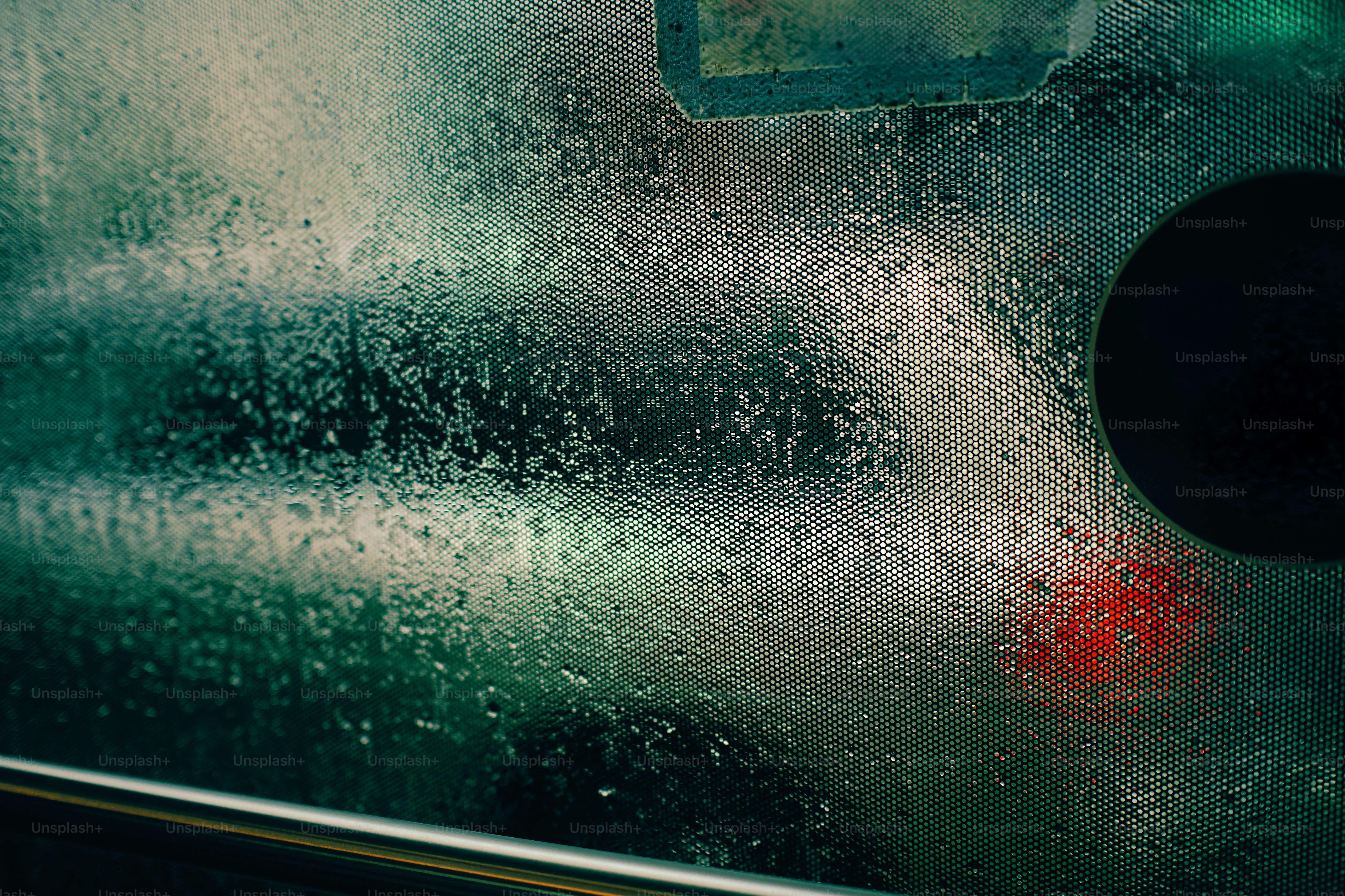 Raindrops on a perforated window film with a blurred red light in the distance