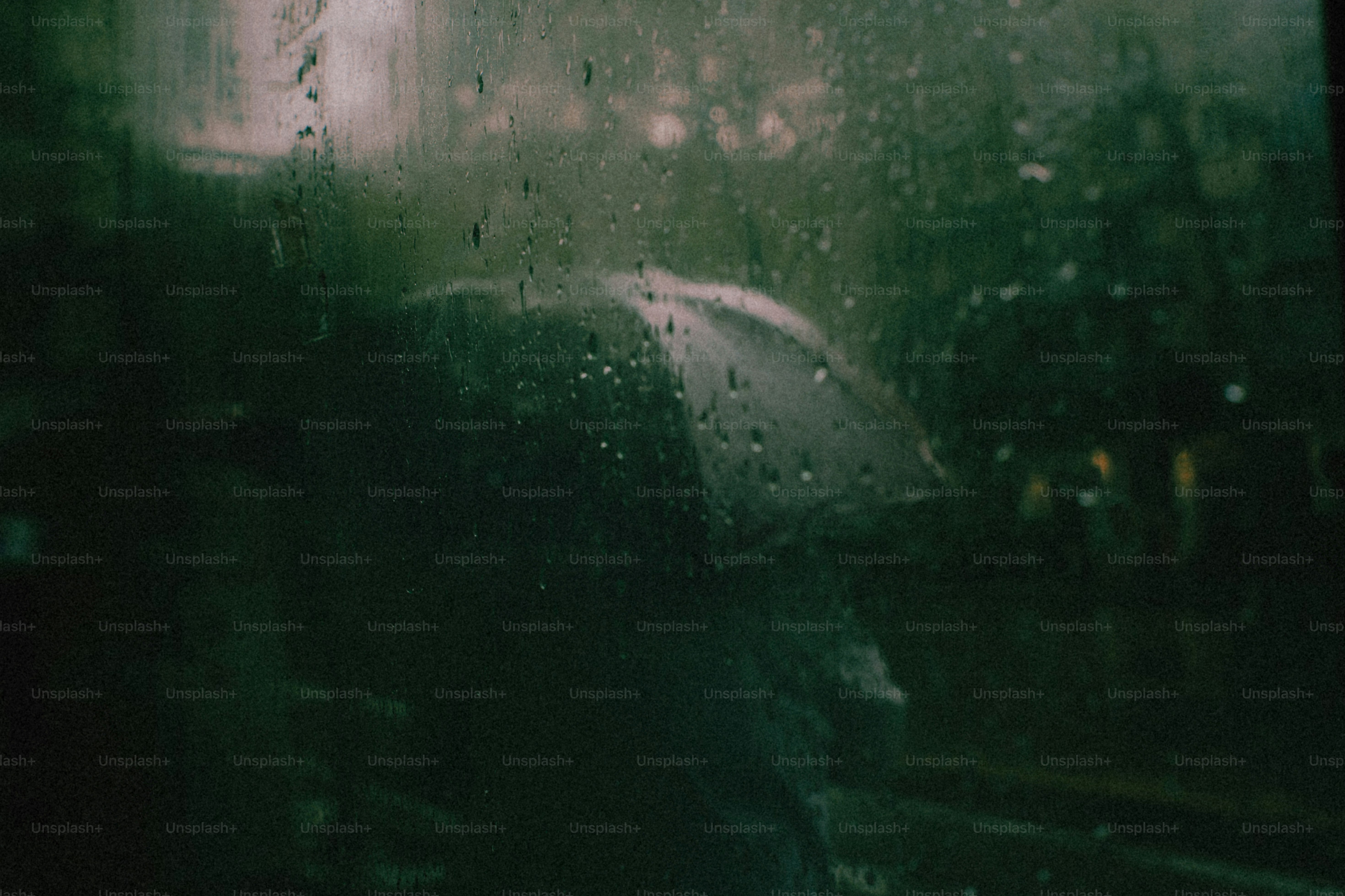 A person holding an umbrella behind a rain-streaked window in dim green light