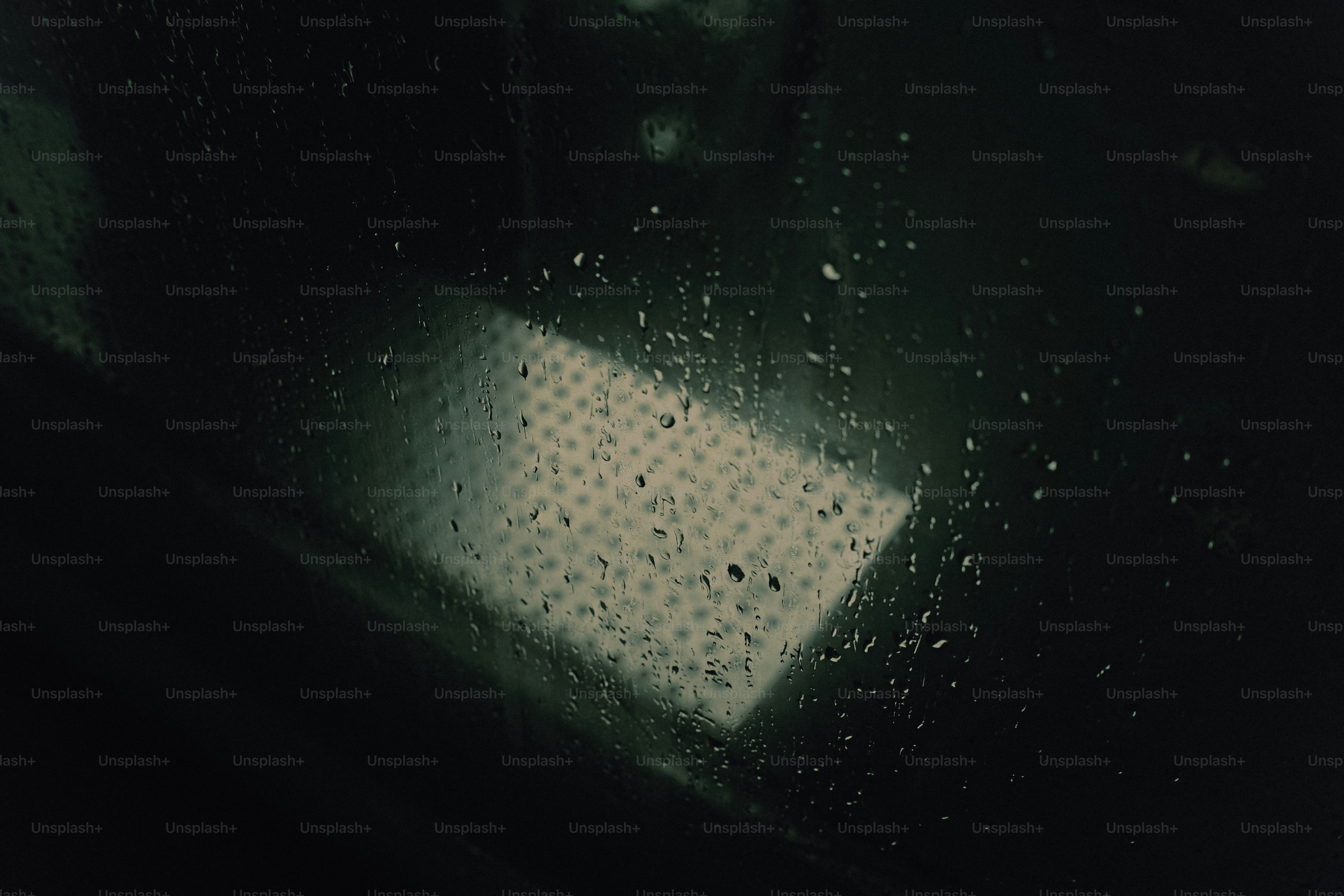 Raindrops on a dark window pane with a glowing grid pattern behind