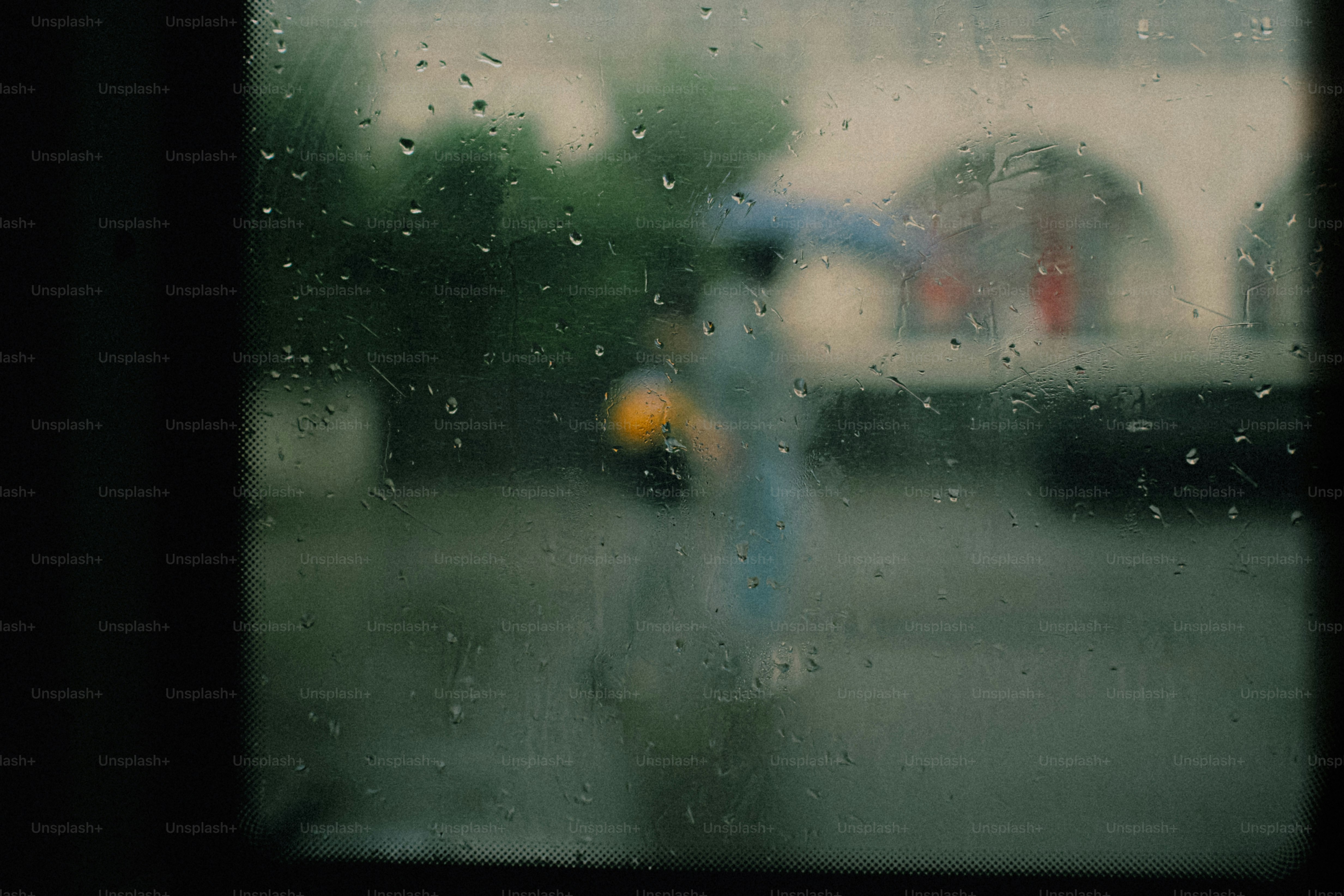 Raindrops on a windowpane with a blurred person holding an umbrella outside