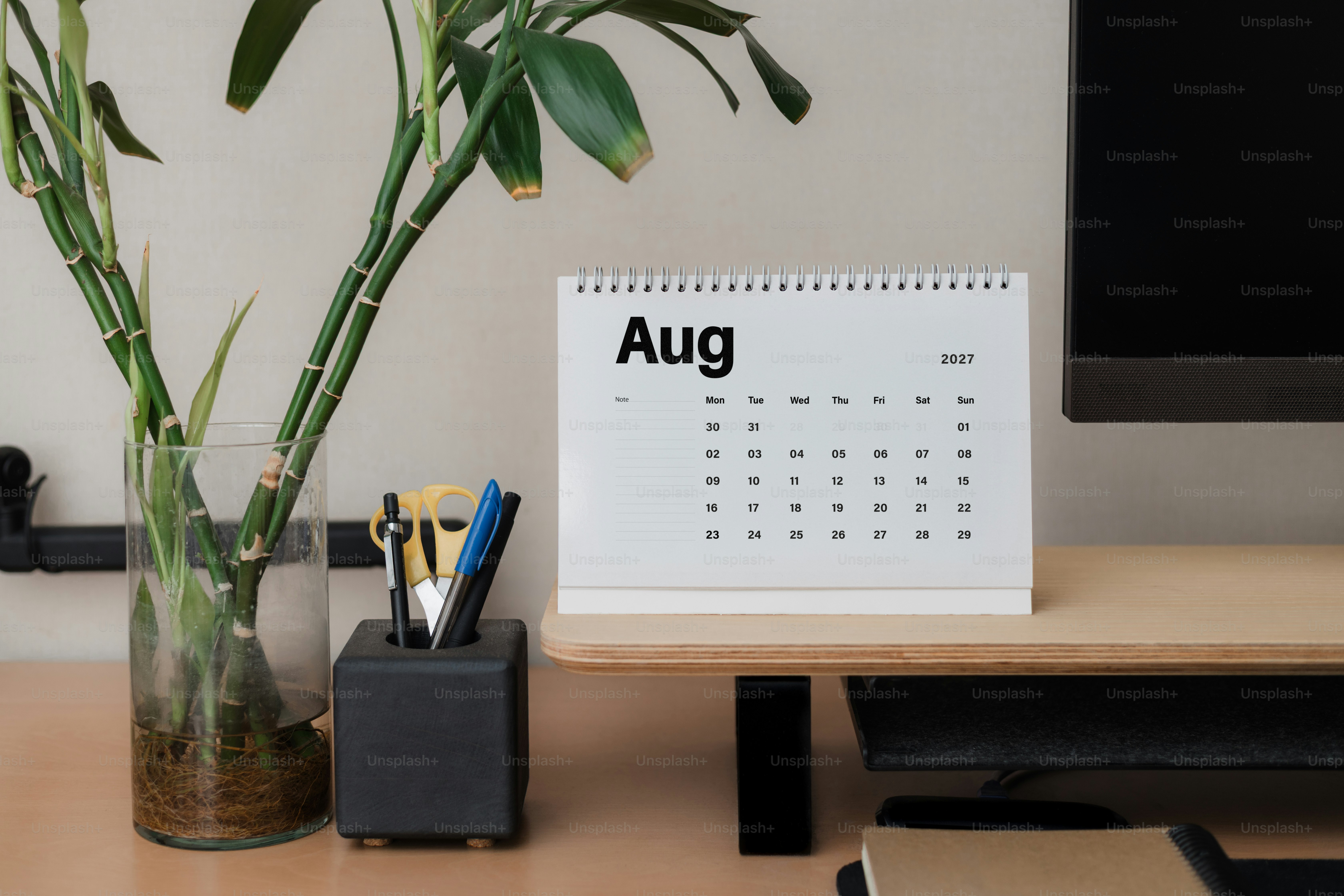 Ein Schreibtischkalender von 2027 zeigt August neben einer Glasvase mit Bambusstielen