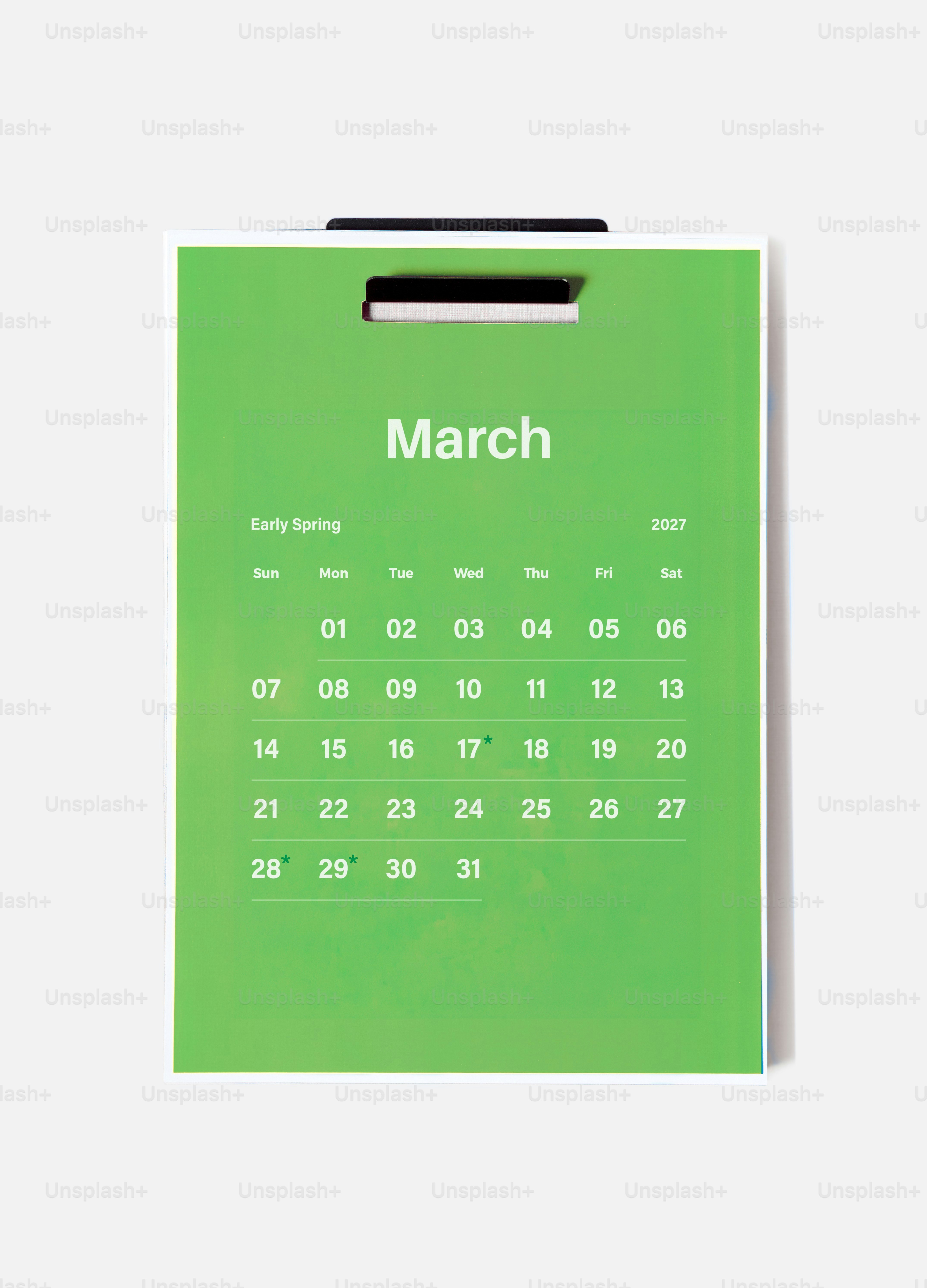 Ein grüner Wandkalender für März 2027, der an einer schlichten weißen Wand hängt