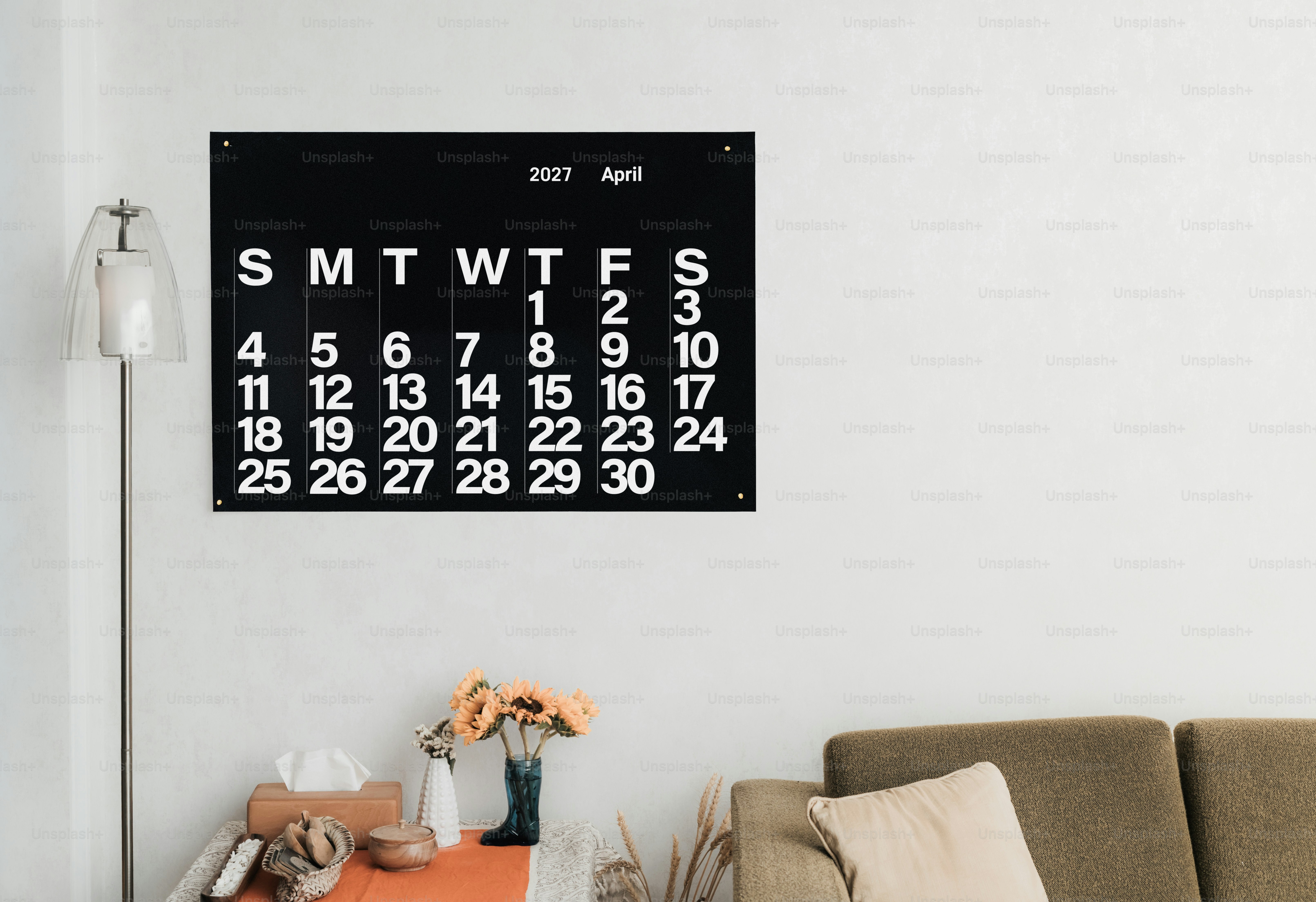 Ein schwarzer Wandkalender für April 2027, der an einer weißen Wand über einem Sofa montiert ist