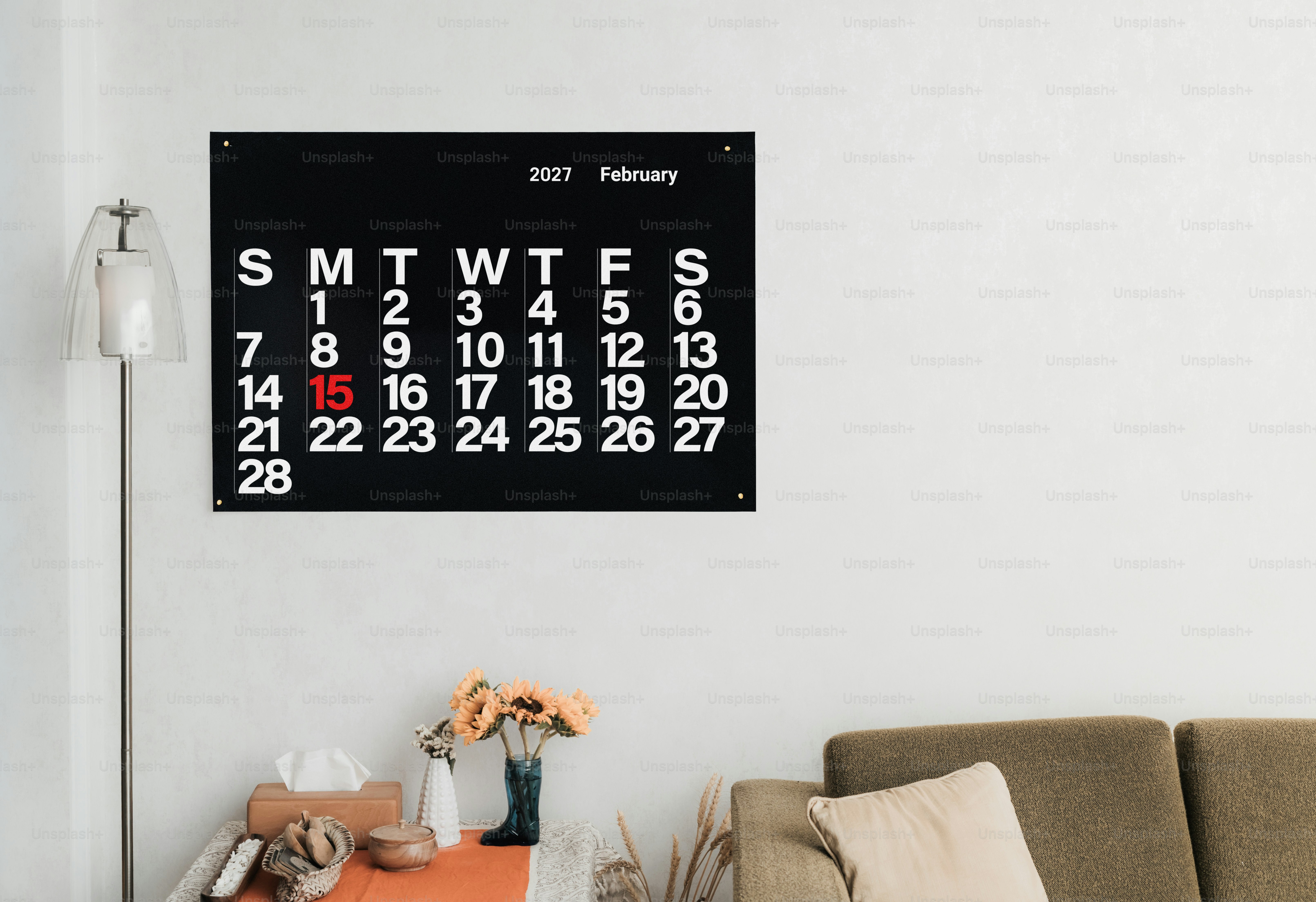 Ein schwarzer Wandkalender für Februar 2027, der über einem Tisch mit Sonnenblumen hängt