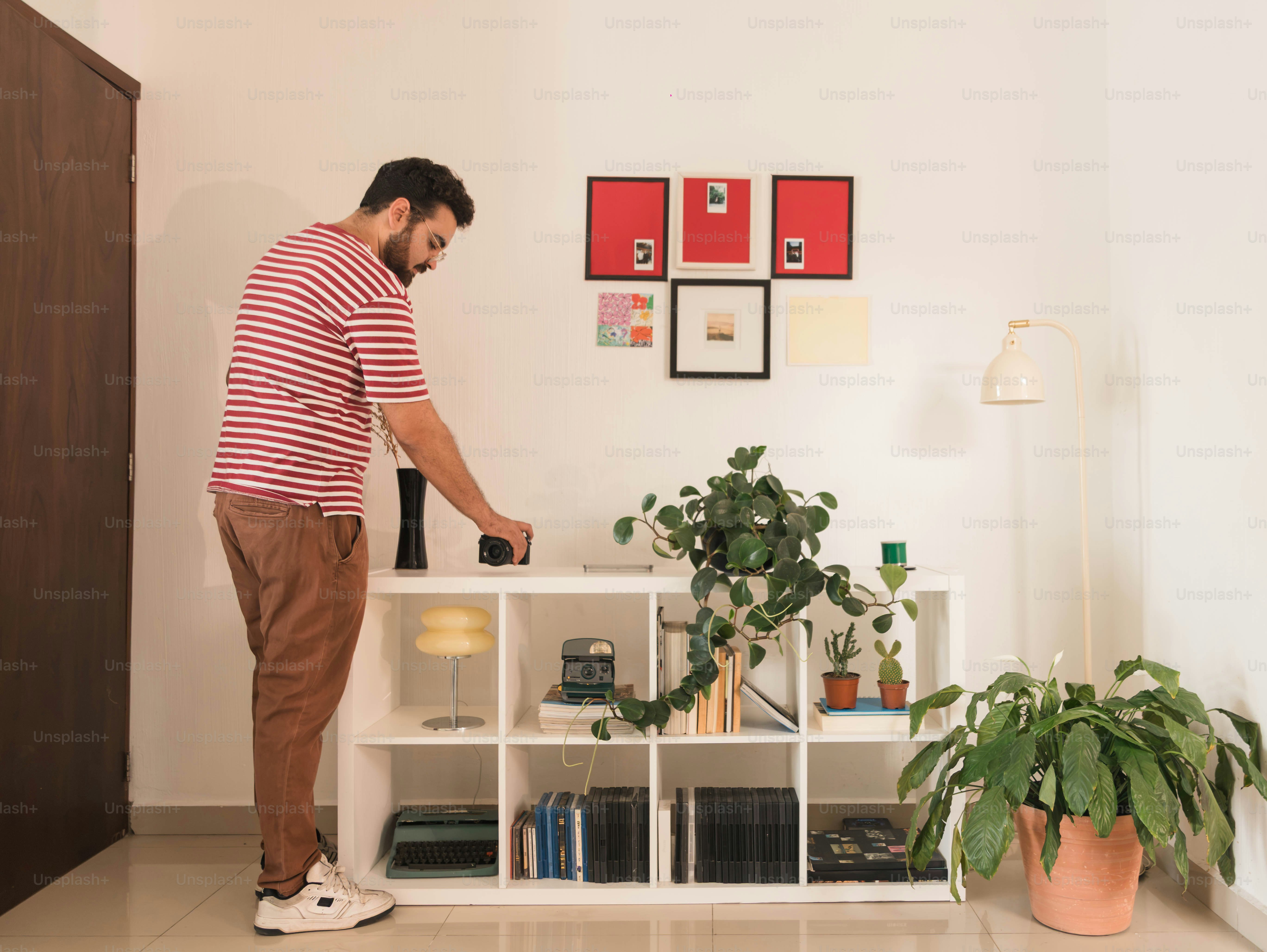 A man in a striped shirt placing a camera on a white shelving unit