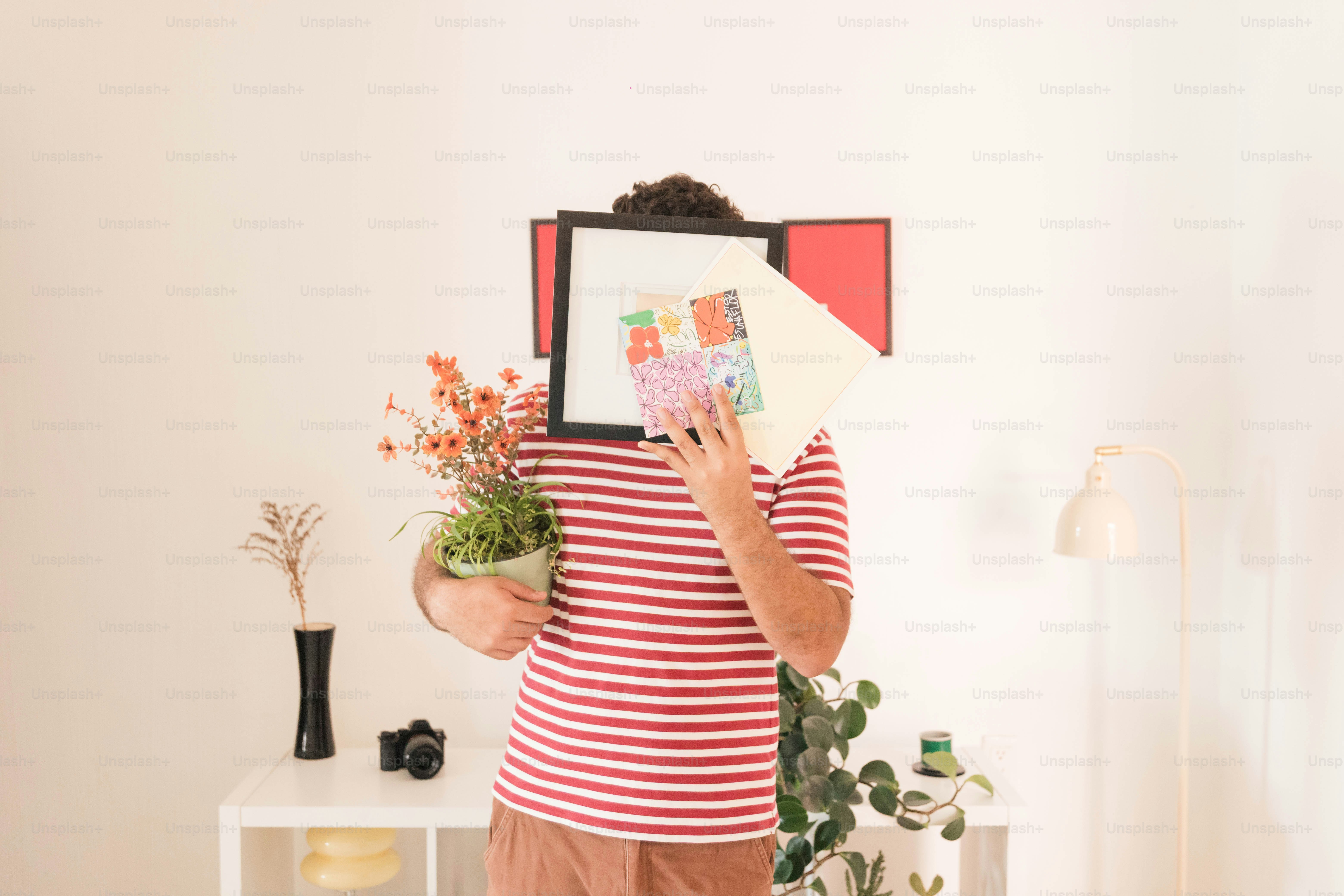 A person in a striped shirt holding a picture frame and a potted plant