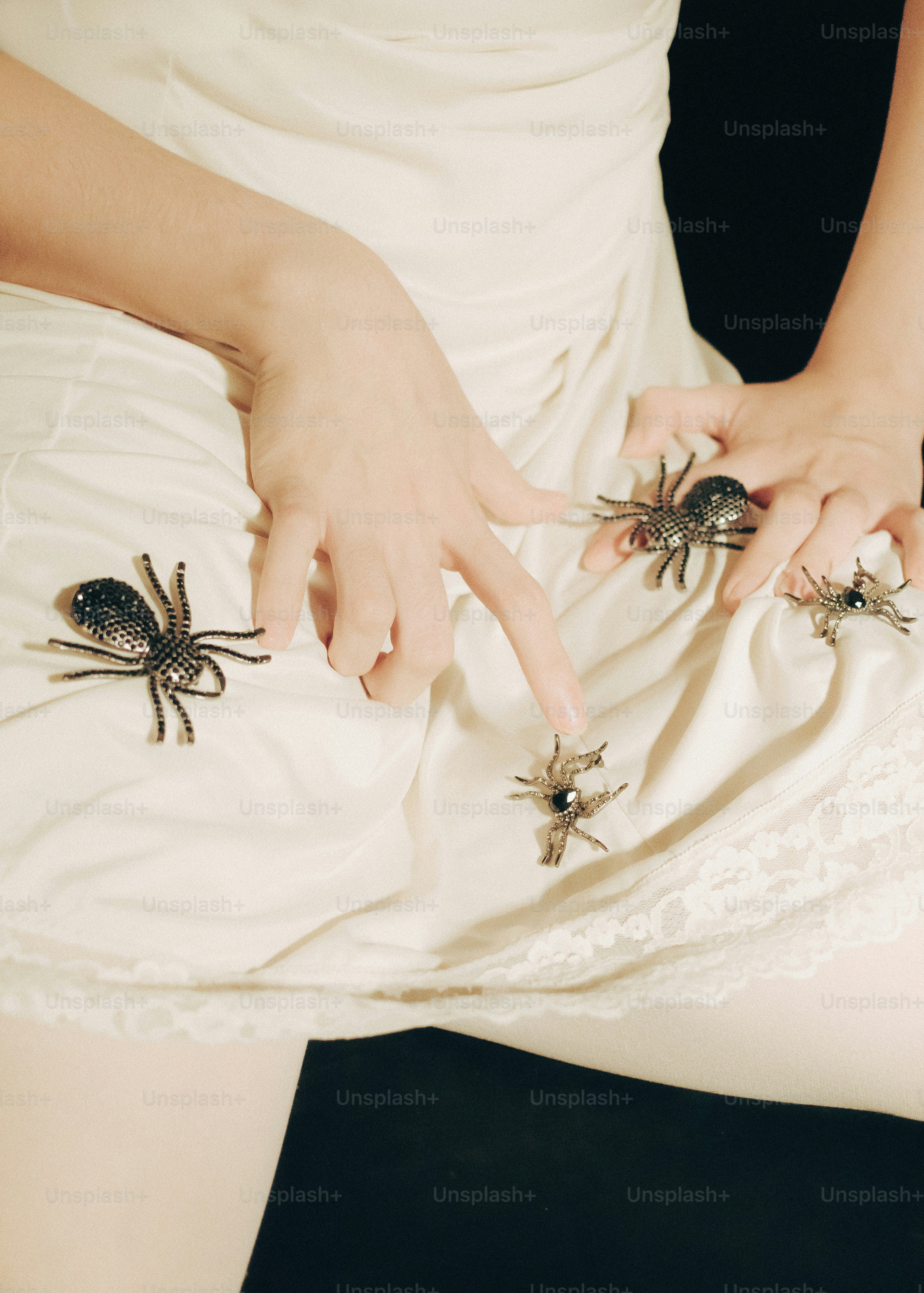 A person wearing a white dress adorned with three decorative spider brooches