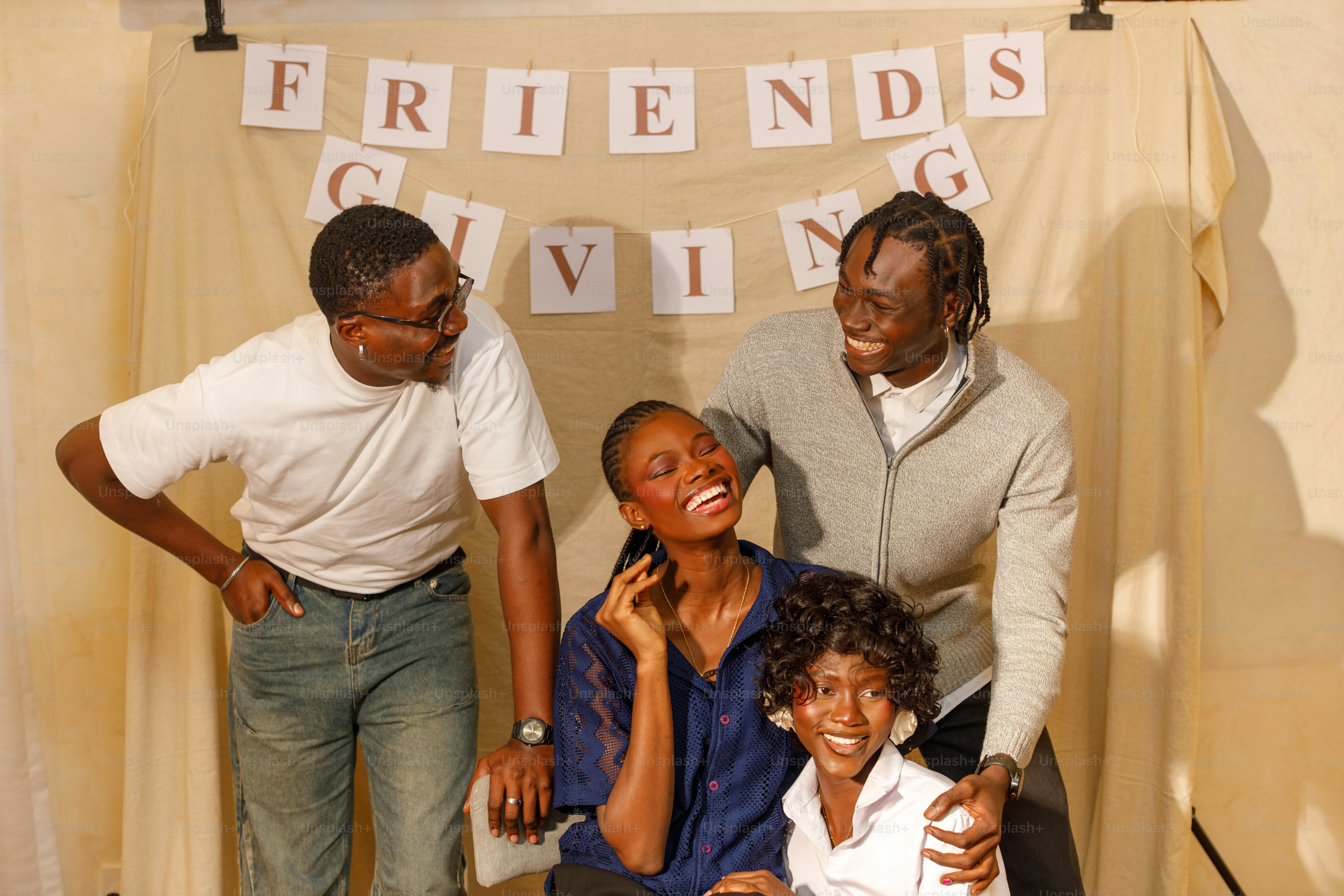 A group of four people laughing in front of a Friendsgiving banner