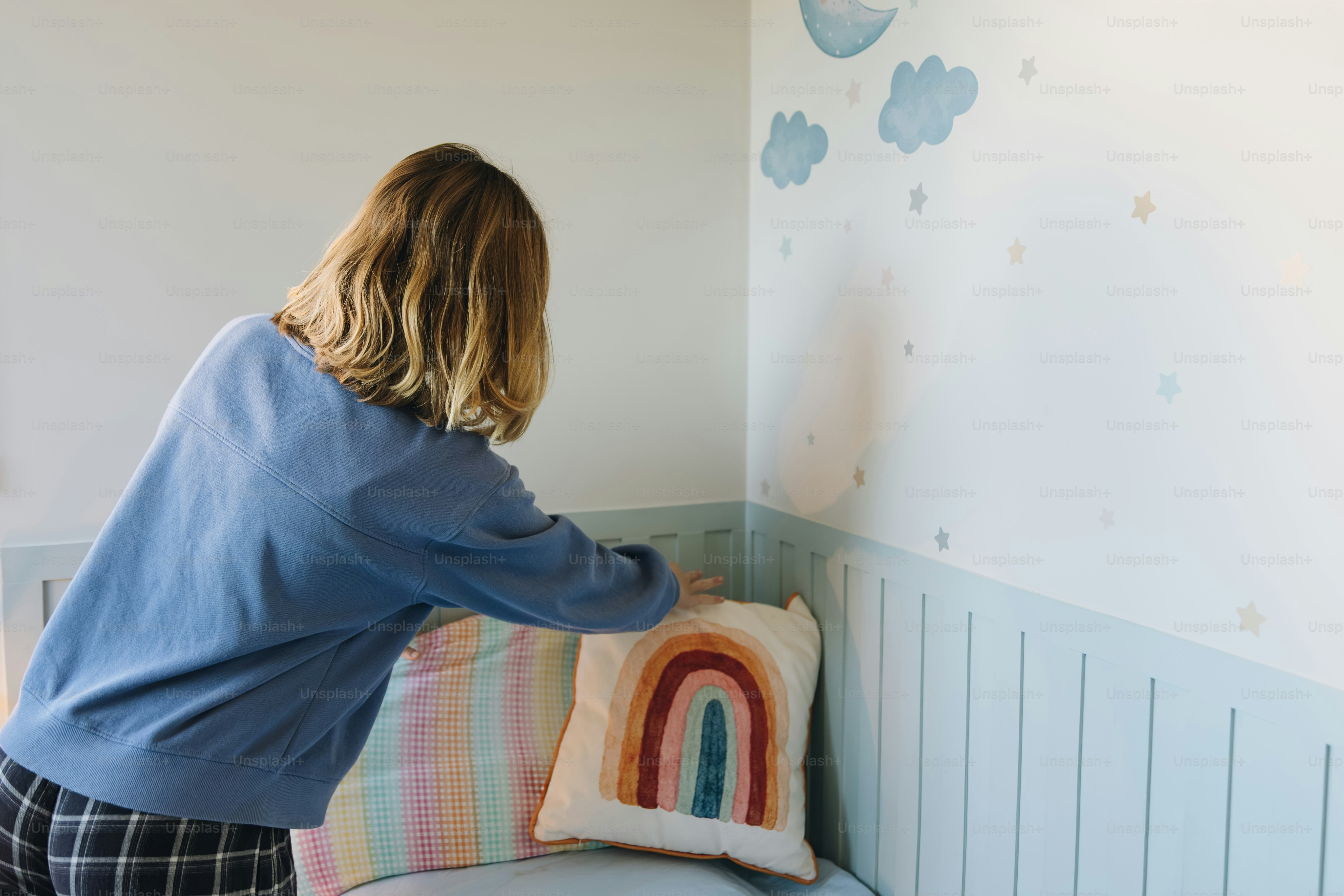 Person adjusting rainbow pillow on bed - Photo on Unsplash+
