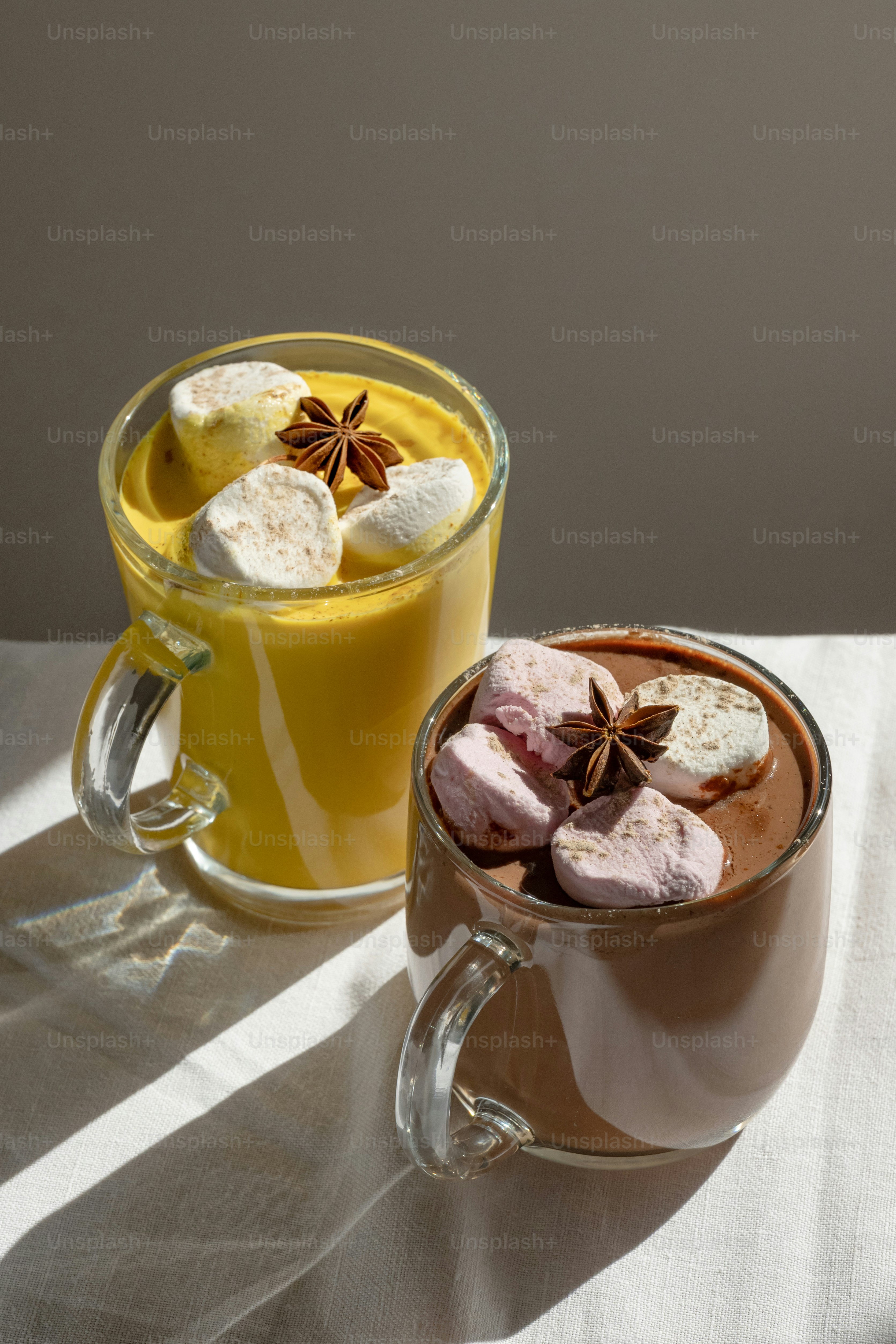 Two glass mugs of hot drinks topped with marshmallows and star anise