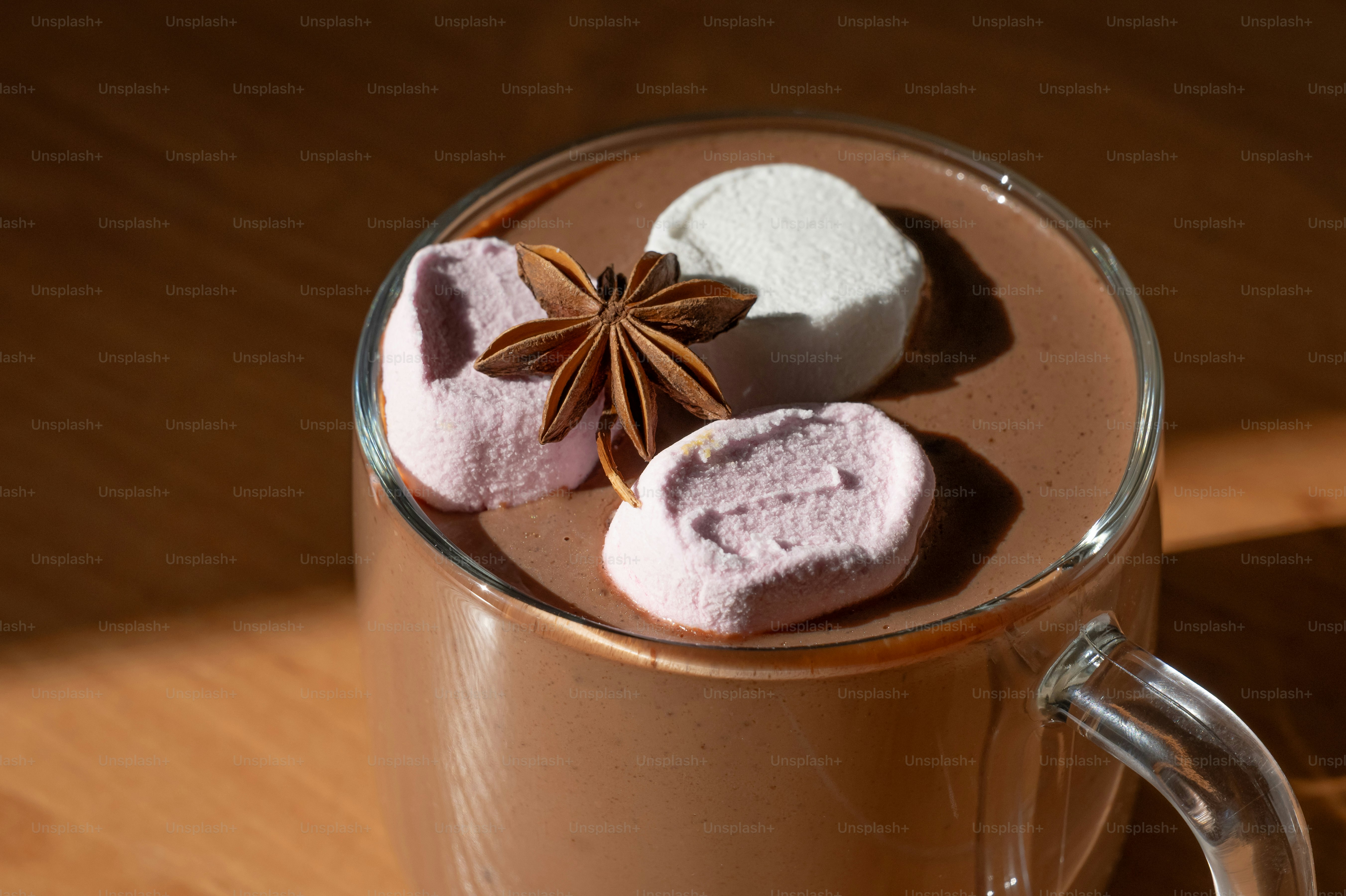 A glass mug of hot chocolate topped with marshmallows and a star anise