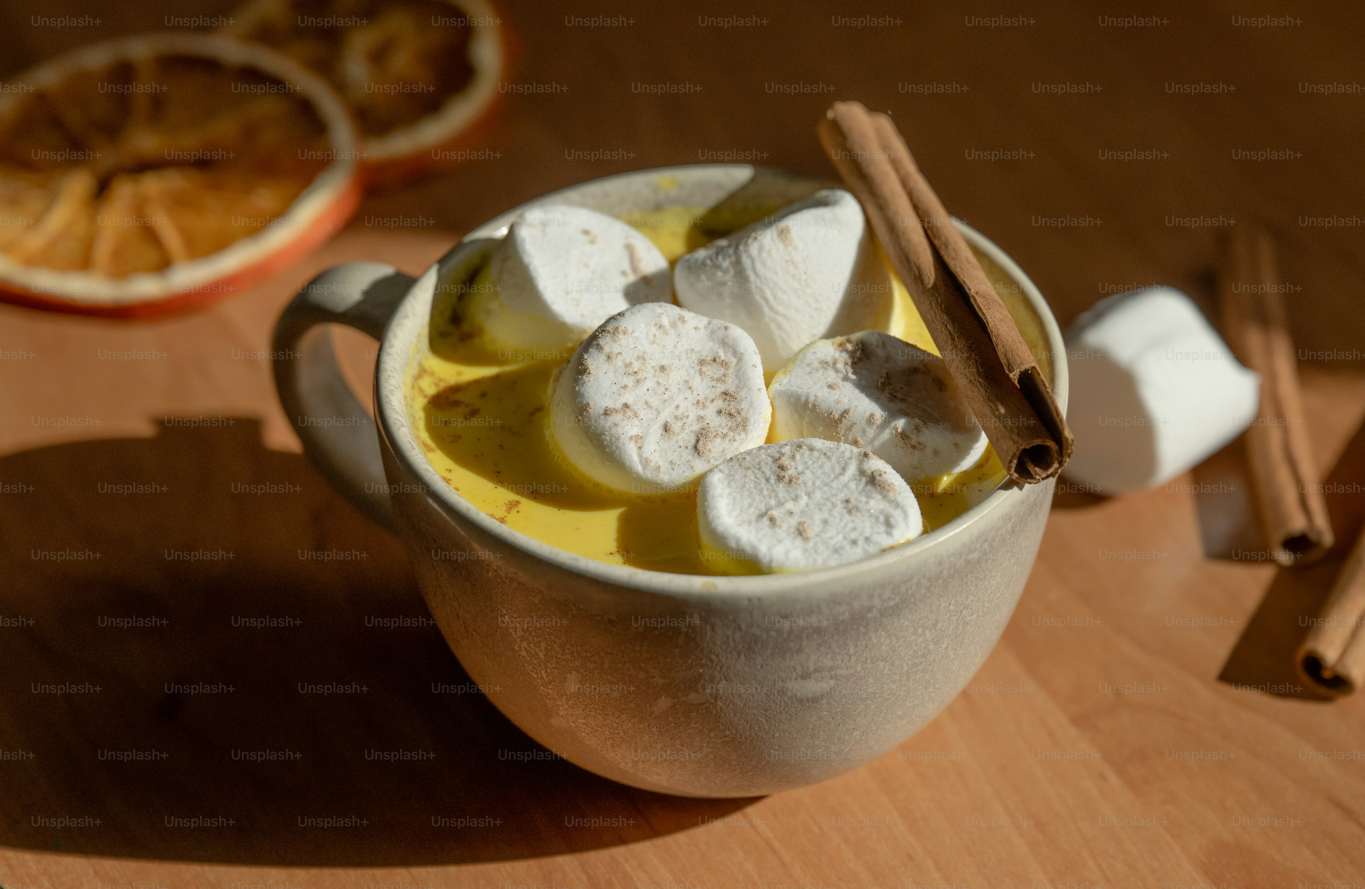 A ceramic mug of yellow drink topped with marshmallows and a cinnamon stick