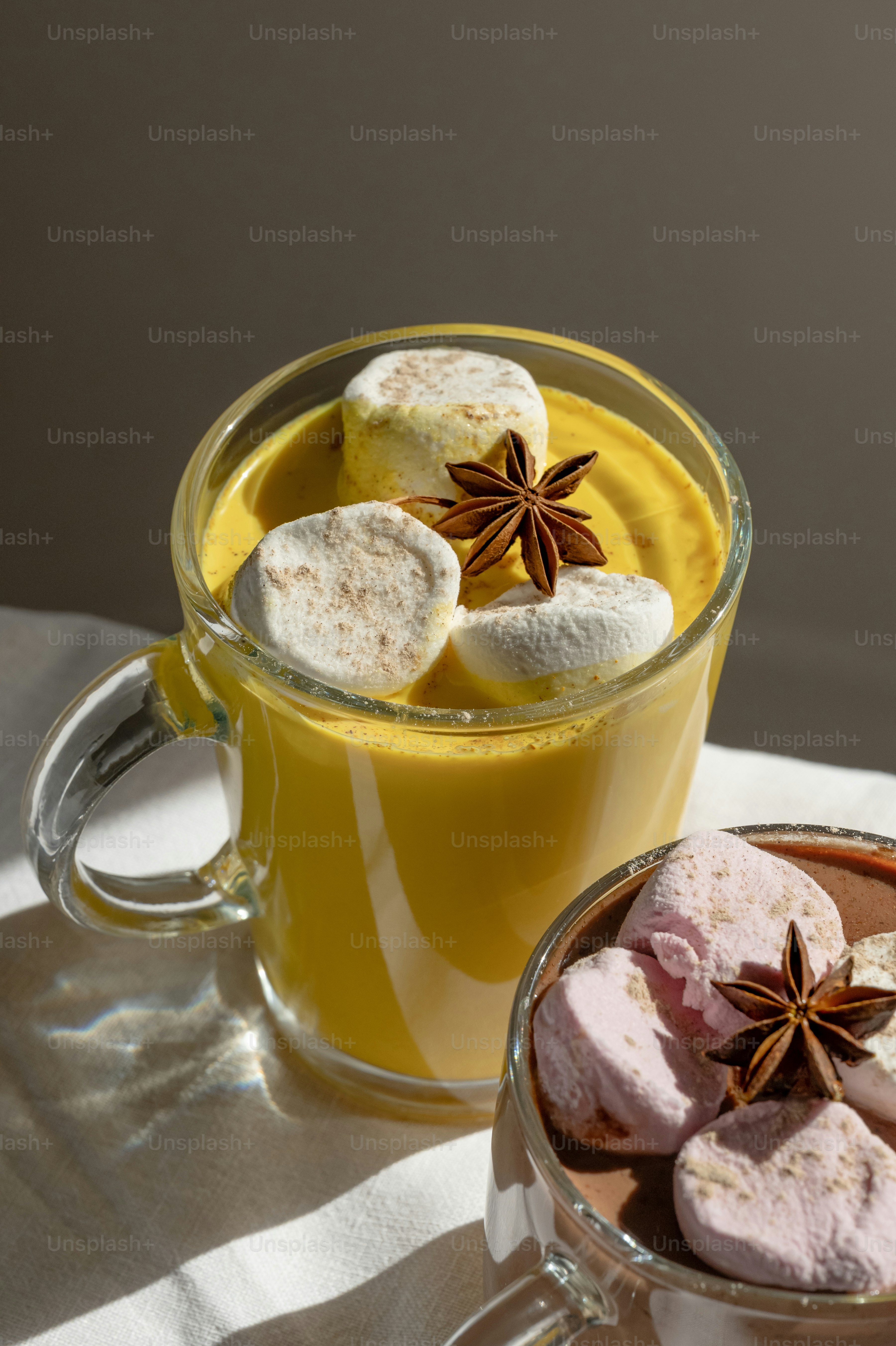 Glass mugs of yellow turmeric latte and cocoa topped with marshmallows and star anise