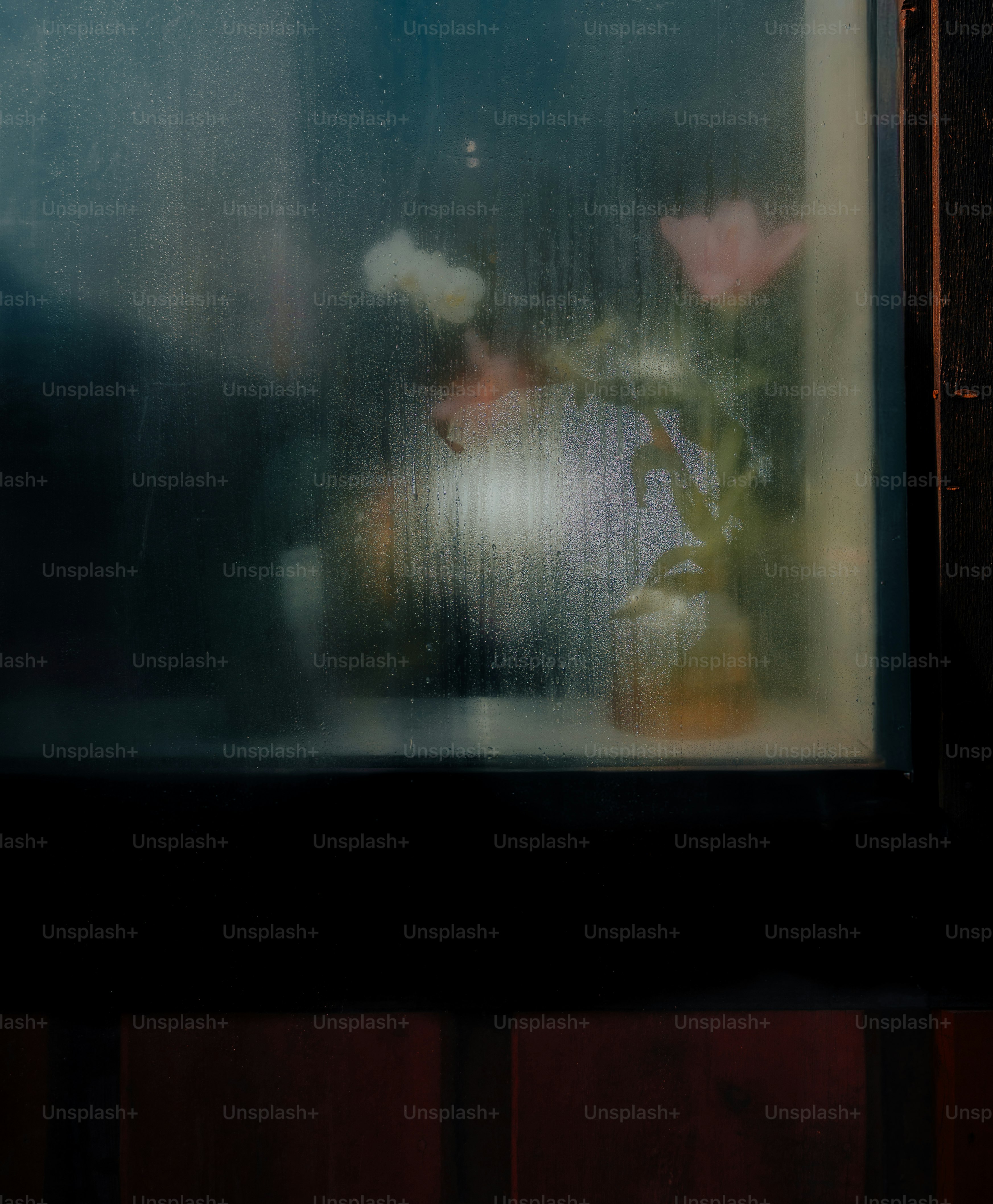 A vase with pink and white flowers behind a rain-streaked window pane