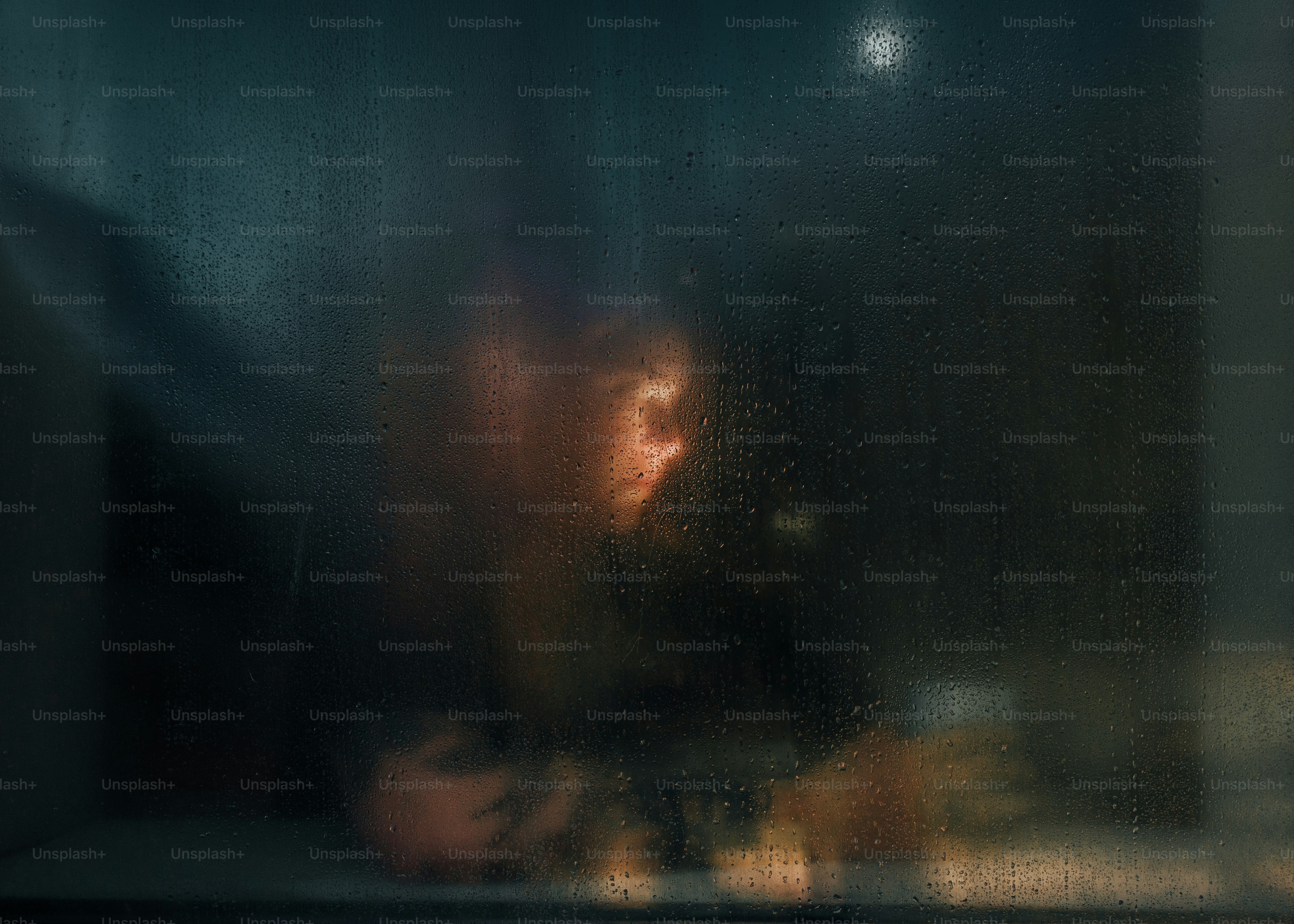 Una persona vista attraverso una finestra bagnata di pioggia di notte con una calda luce interna
