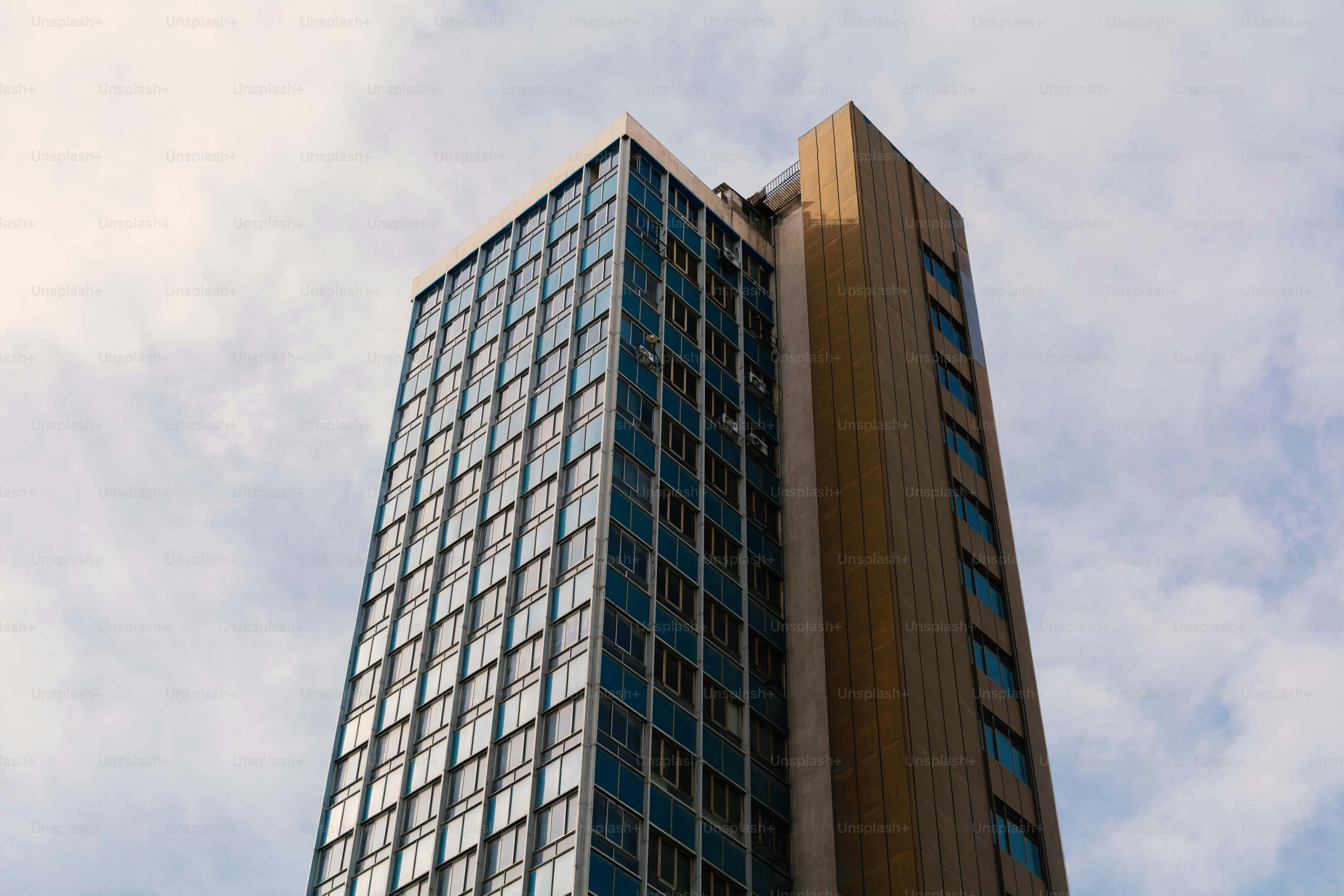 Ein hoher Wolkenkratzer mit blauen Glasfenstern und einer goldenen Metallfassade gegen Wolken