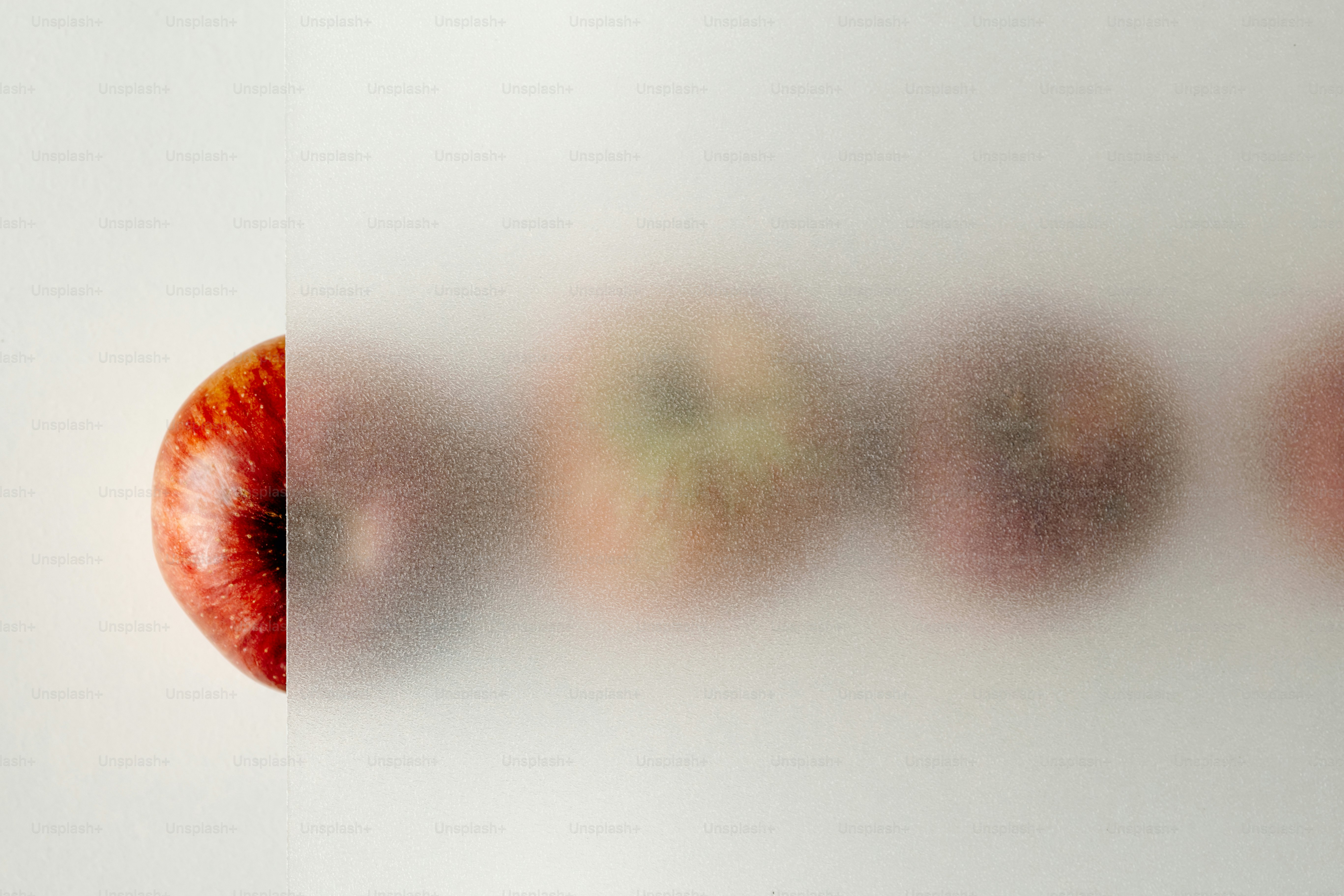 A red apple partially obscured by a translucent frosted glass pane