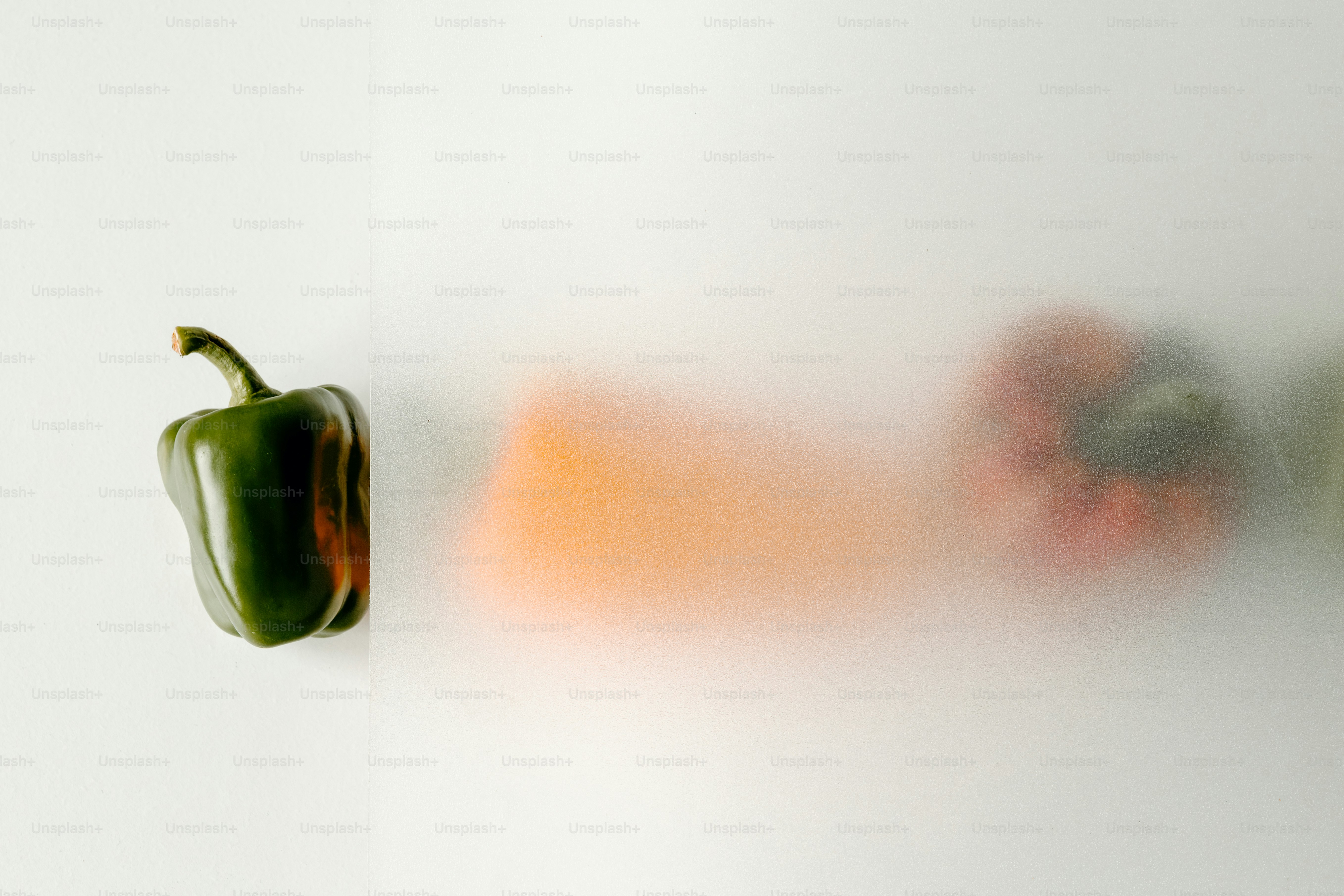 A green bell pepper beside a blurred red pepper behind frosted glass