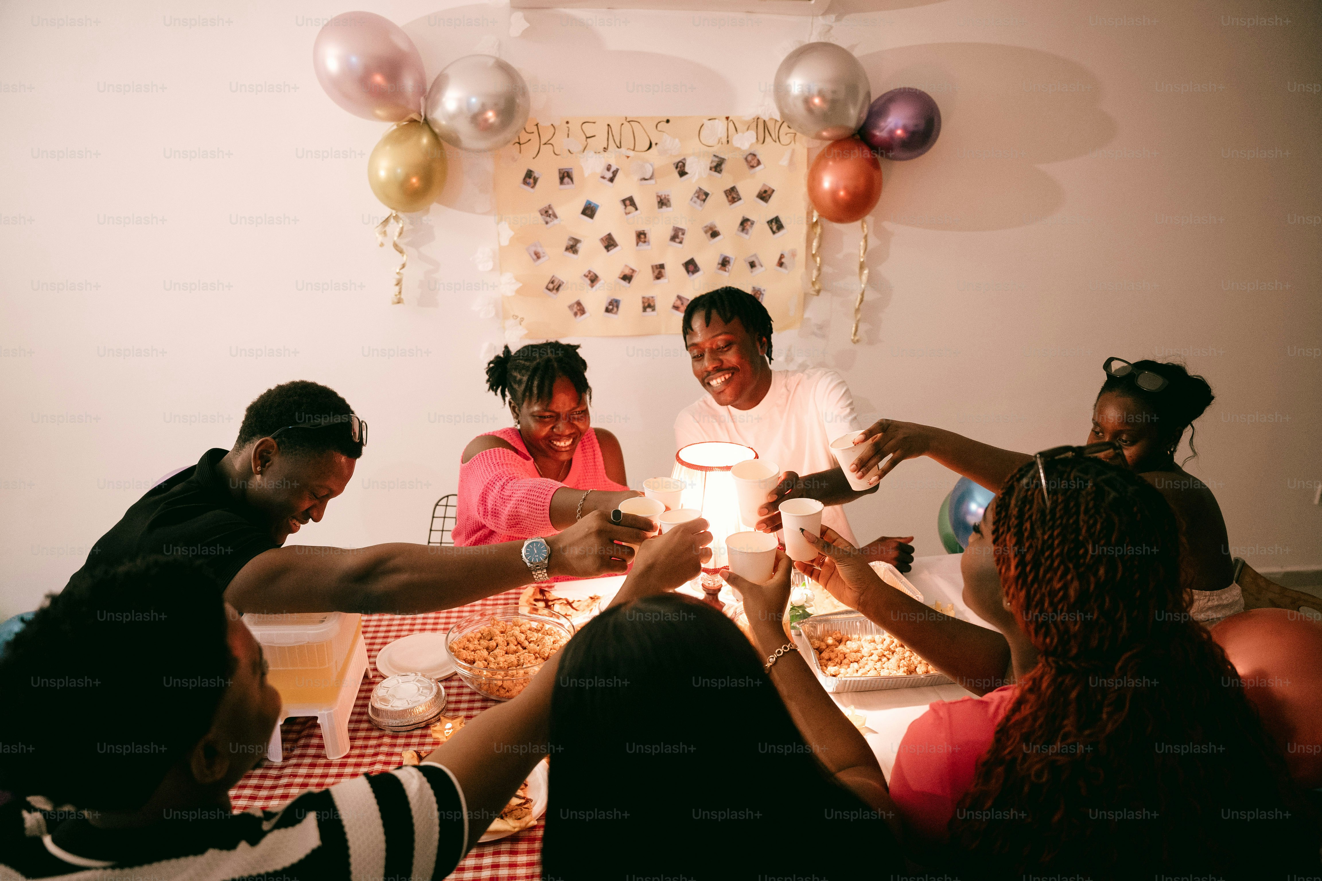 A group of people toasting with paper cups at a table with snacks