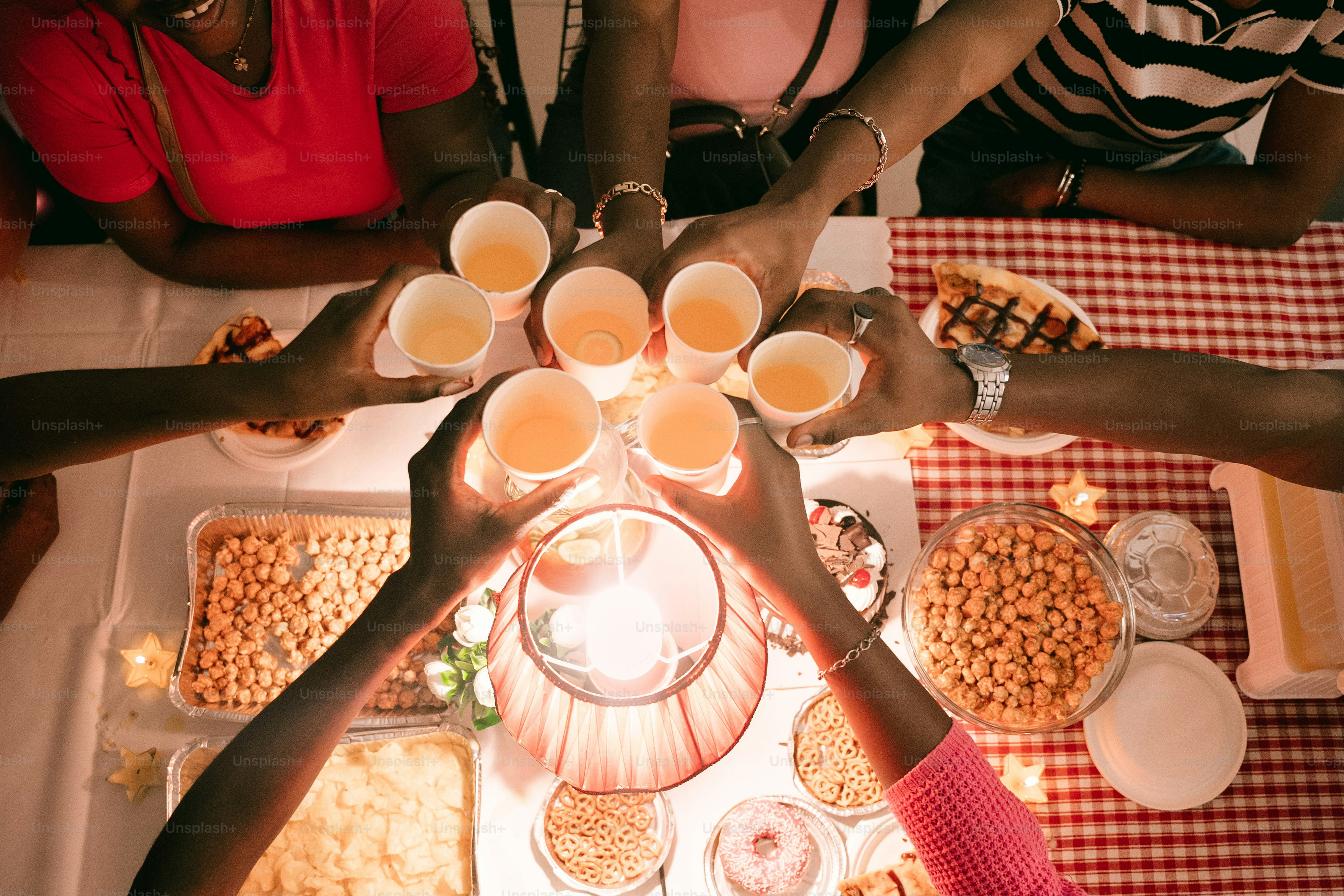 A group of people toasting with paper cups over a table of food