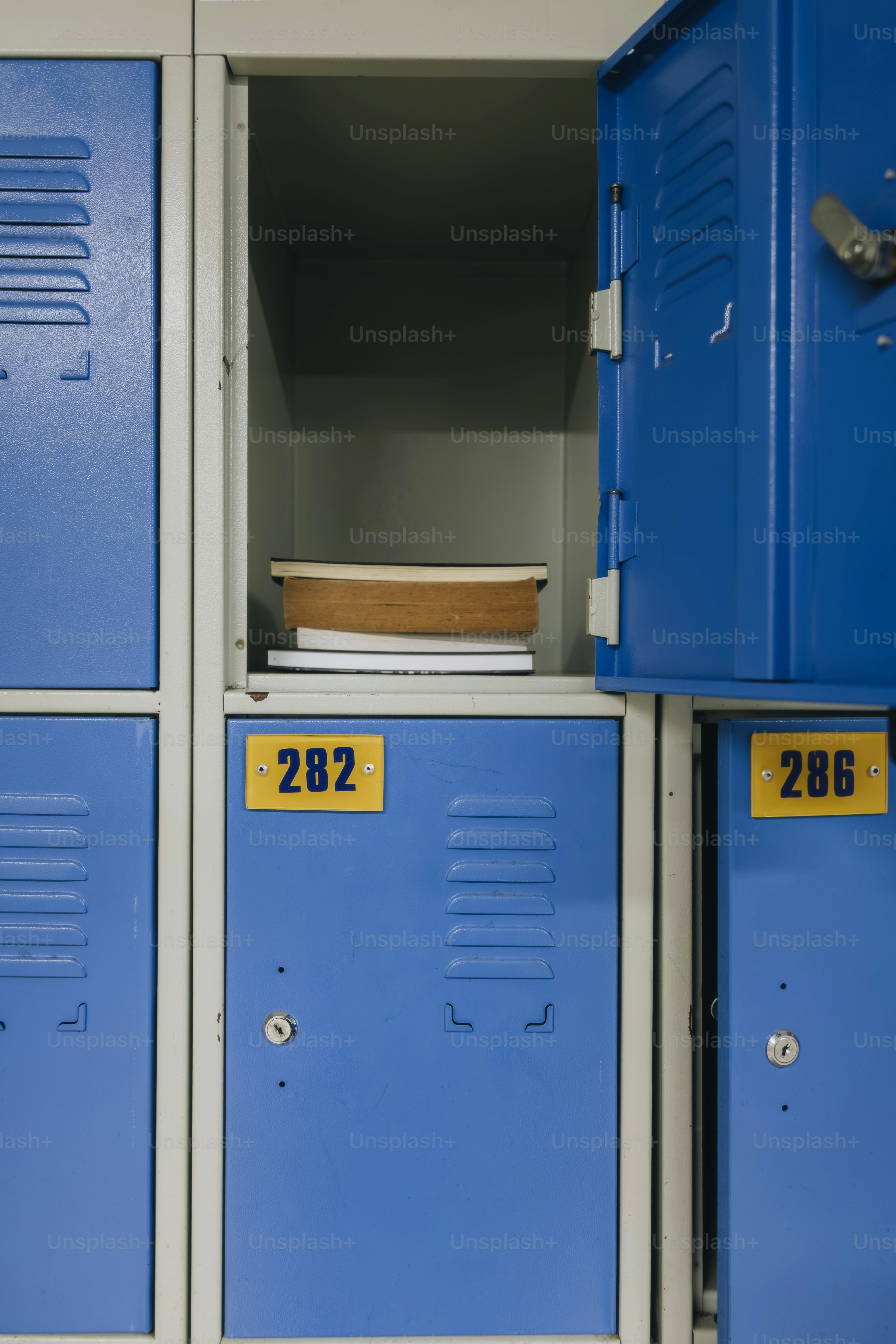 Ein Stapel Bücher in einem offenen blauen Metallschließfach mit der Nummer 282