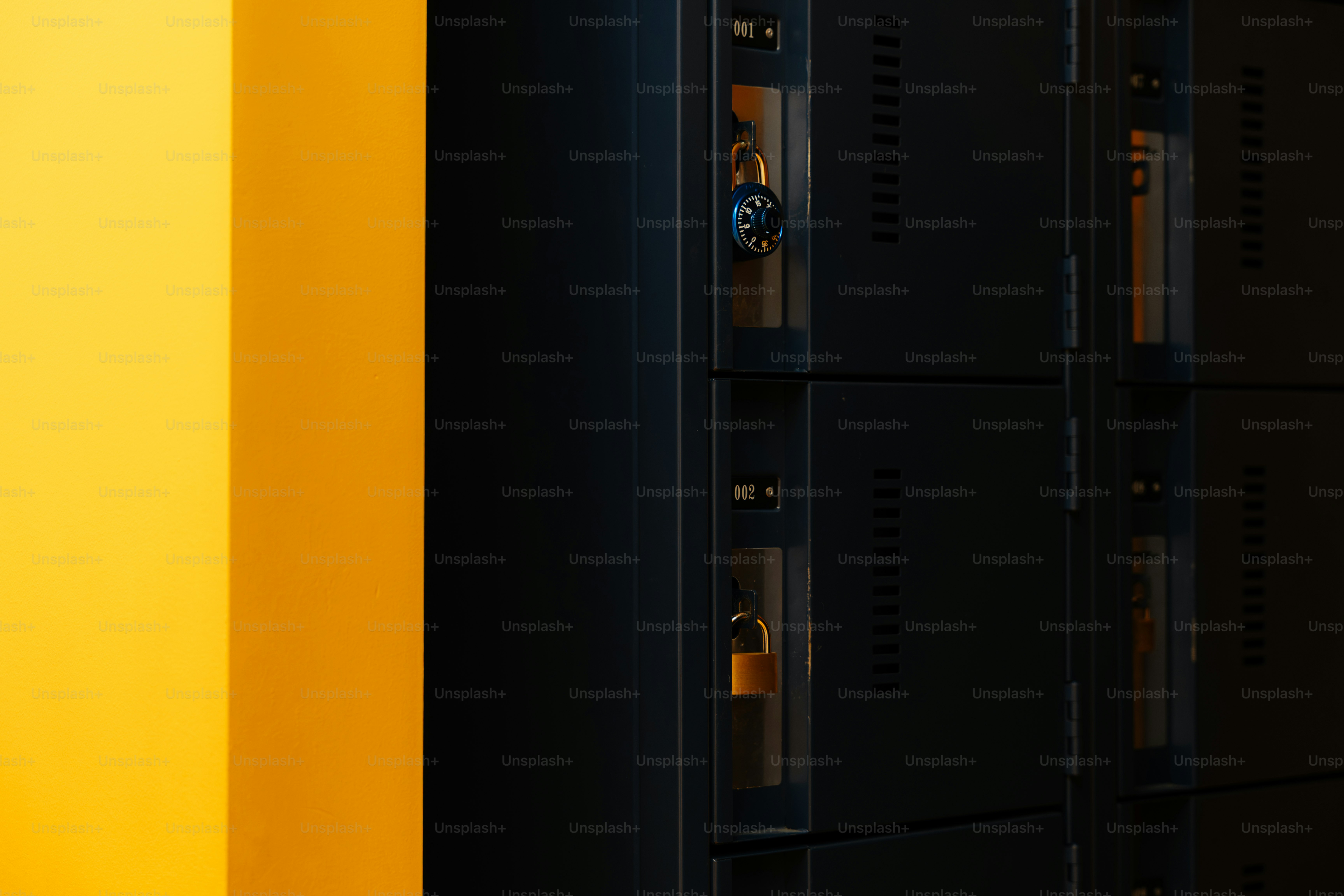 Des casiers métalliques sombres avec des cadenas à côté d’un mur jaune vif