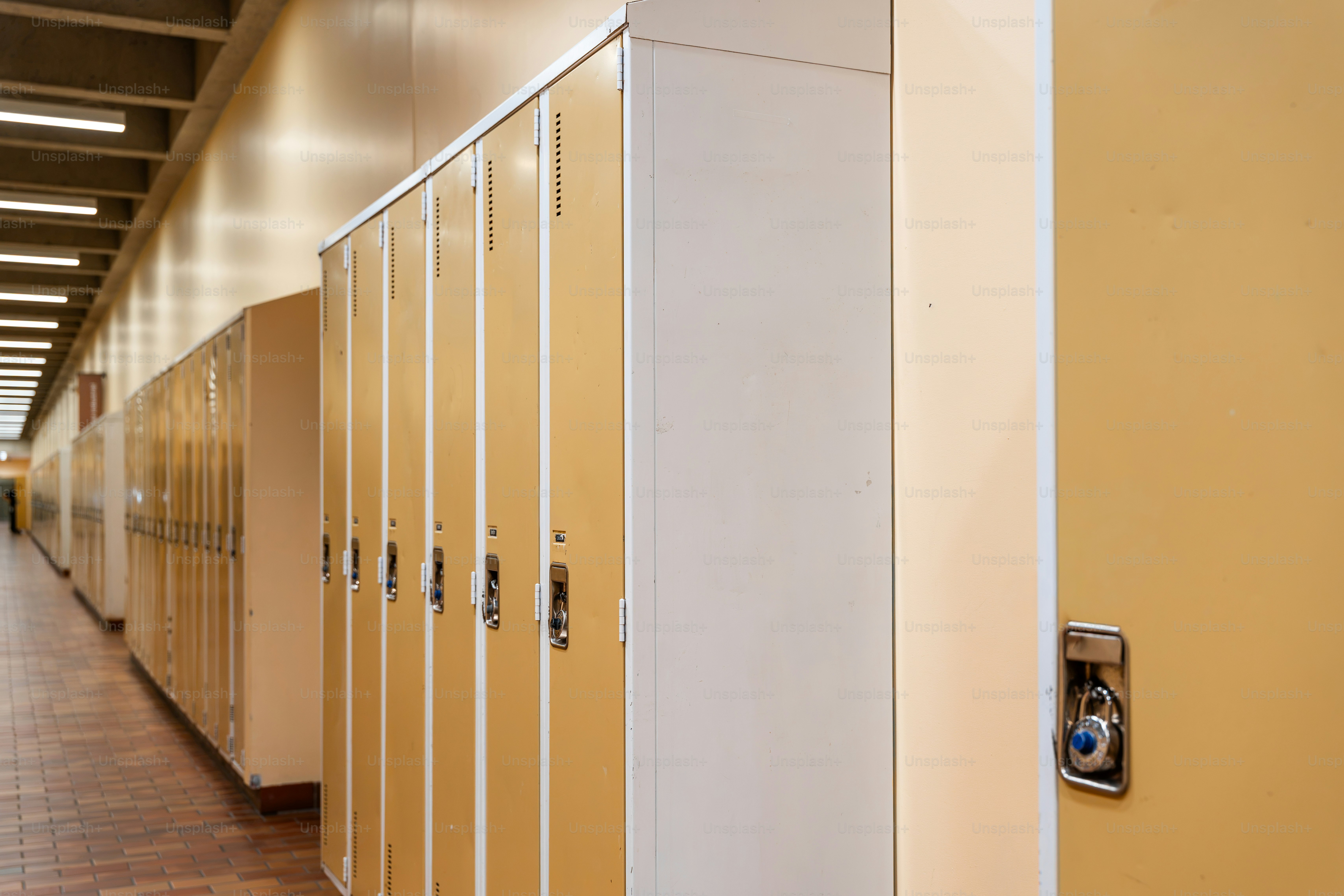 Une longue rangée de casiers métalliques jaunes dans un couloir d’école aux sols carrelés