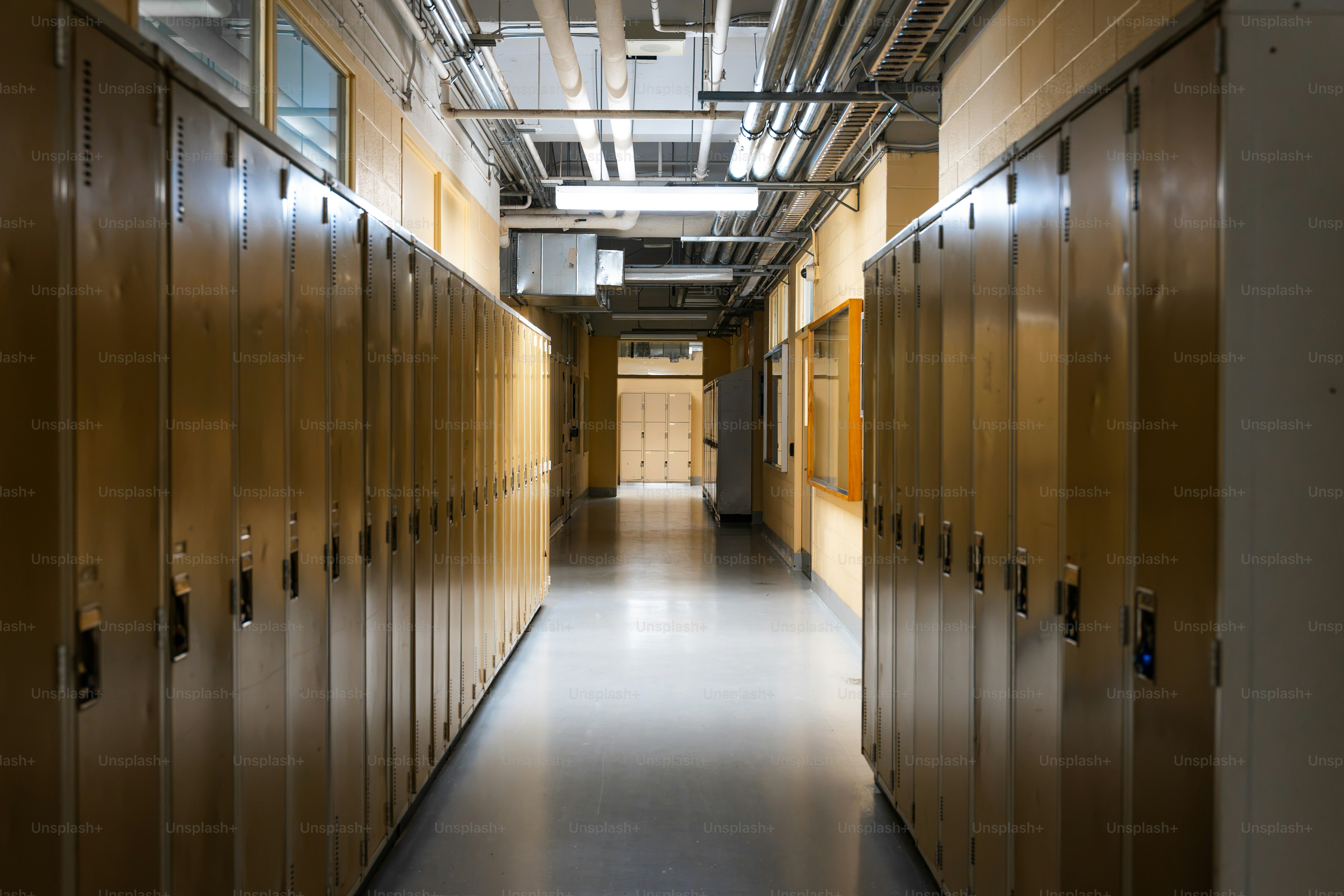 Un long couloir d’école bordé de rangées de casiers métalliques et de tuyaux de plafond apparents