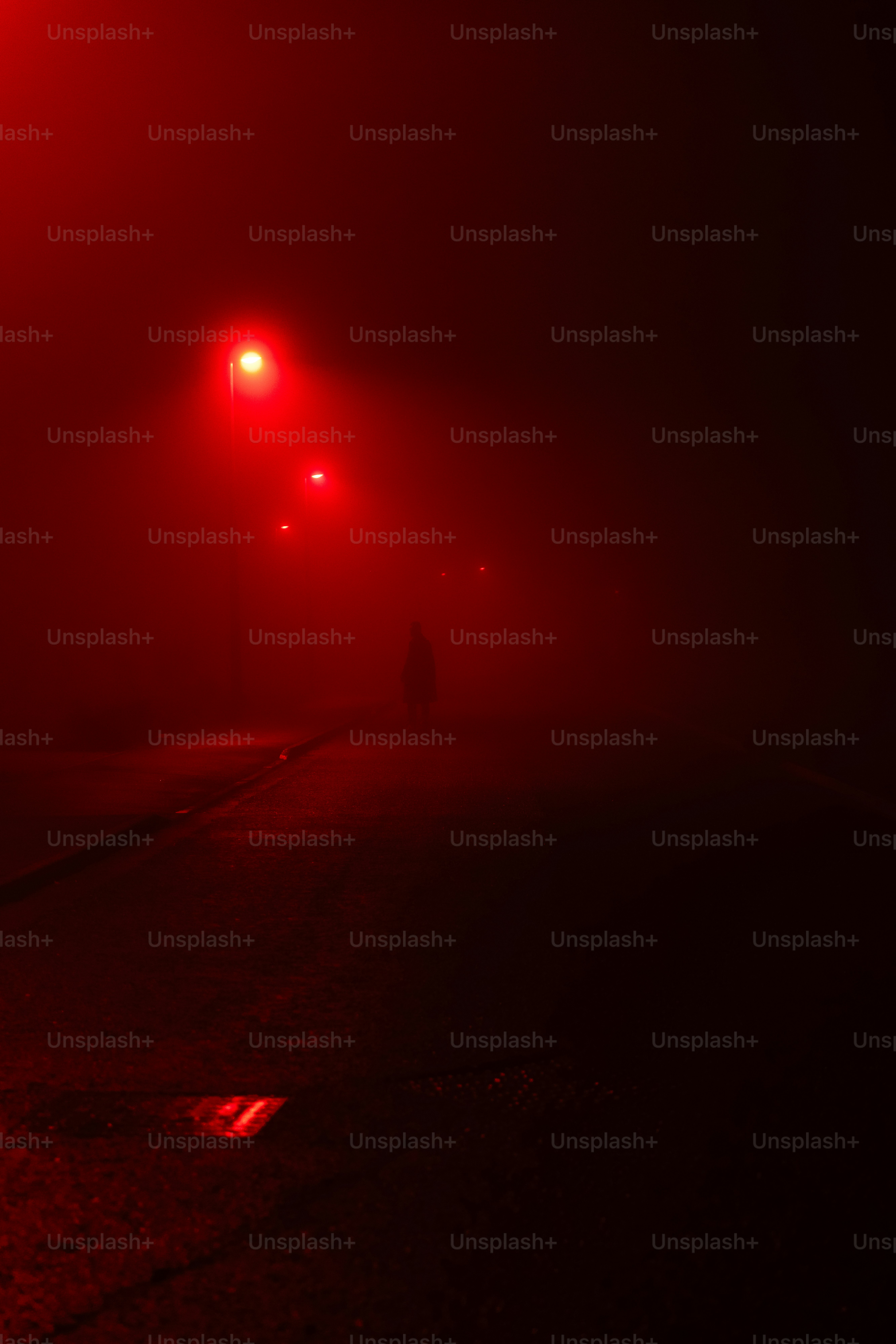 Una persona solitaria che cammina su una strada buia illuminata da lampioni rossi nella nebbia